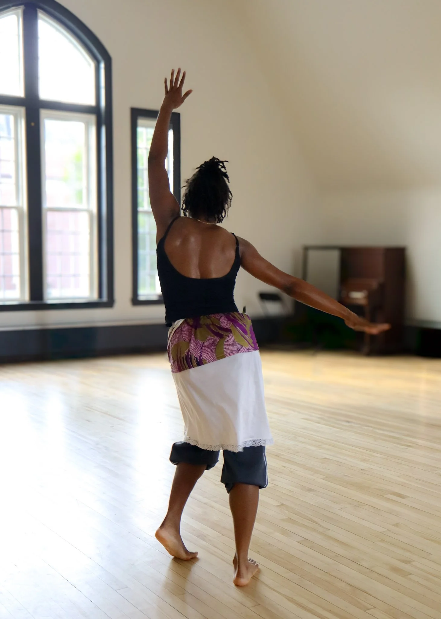 A person with short dark hair dancing or performing in a spacious room with large windows and wooden floors.