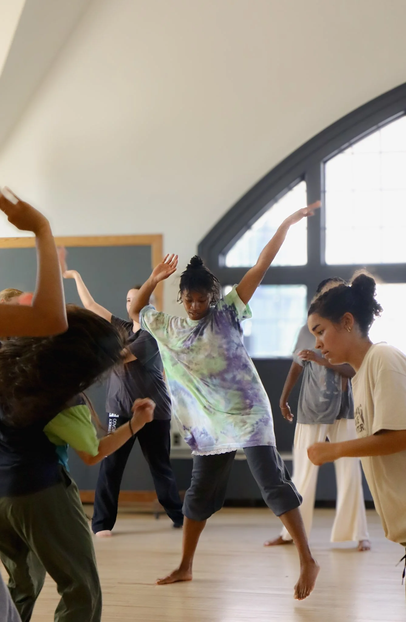 Group of diverse people practicing yoga or a dance in a studio with large windows and wooden floor.