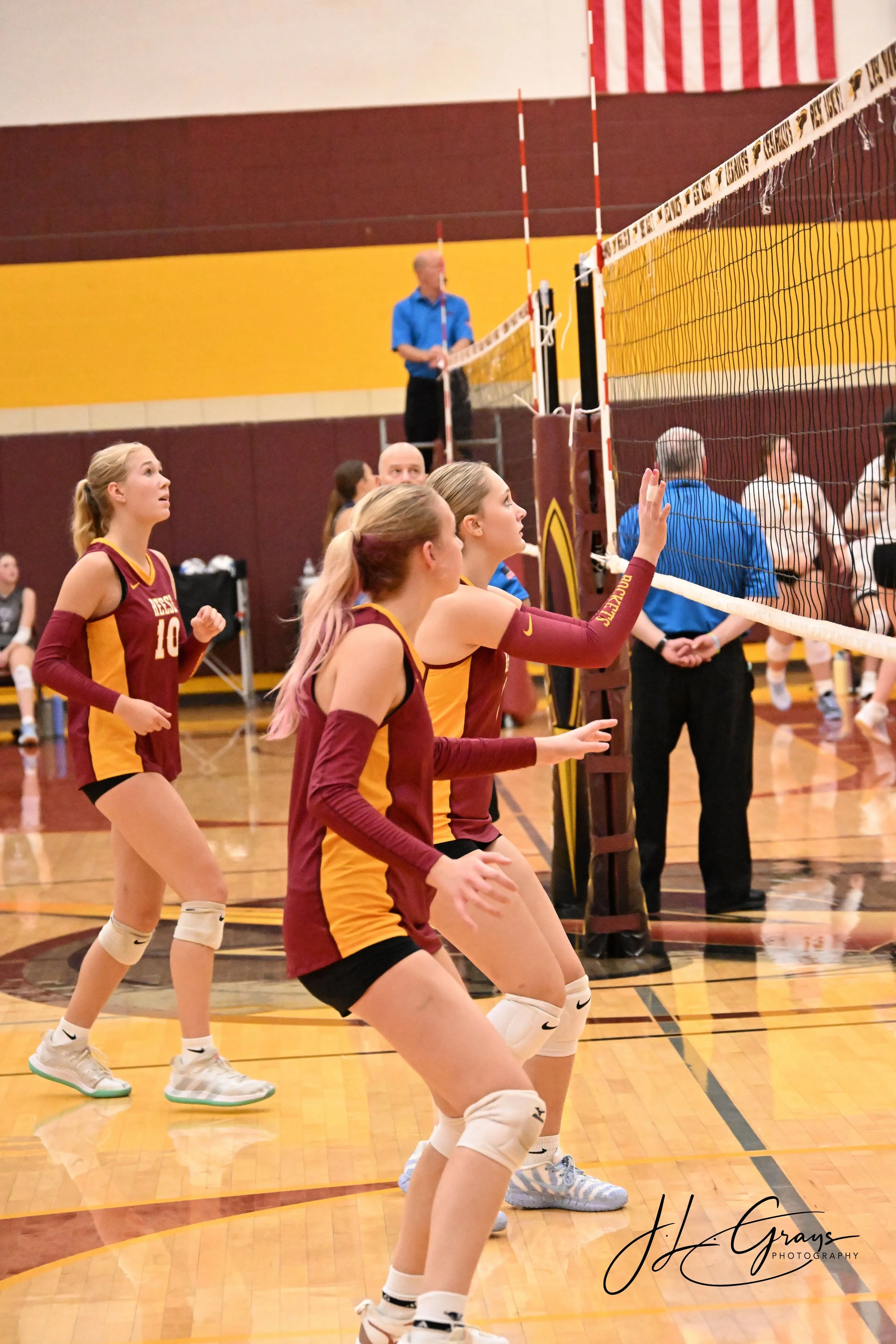 Volleyball players in maroon and yellow jerseys on the court during a match.