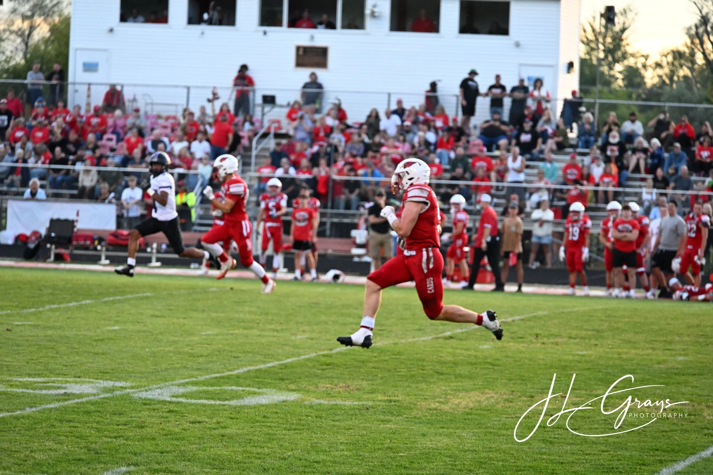 American football game with players in red and white jerseys on the field during the evening, spectators sitting in the bleachers and watching the game.