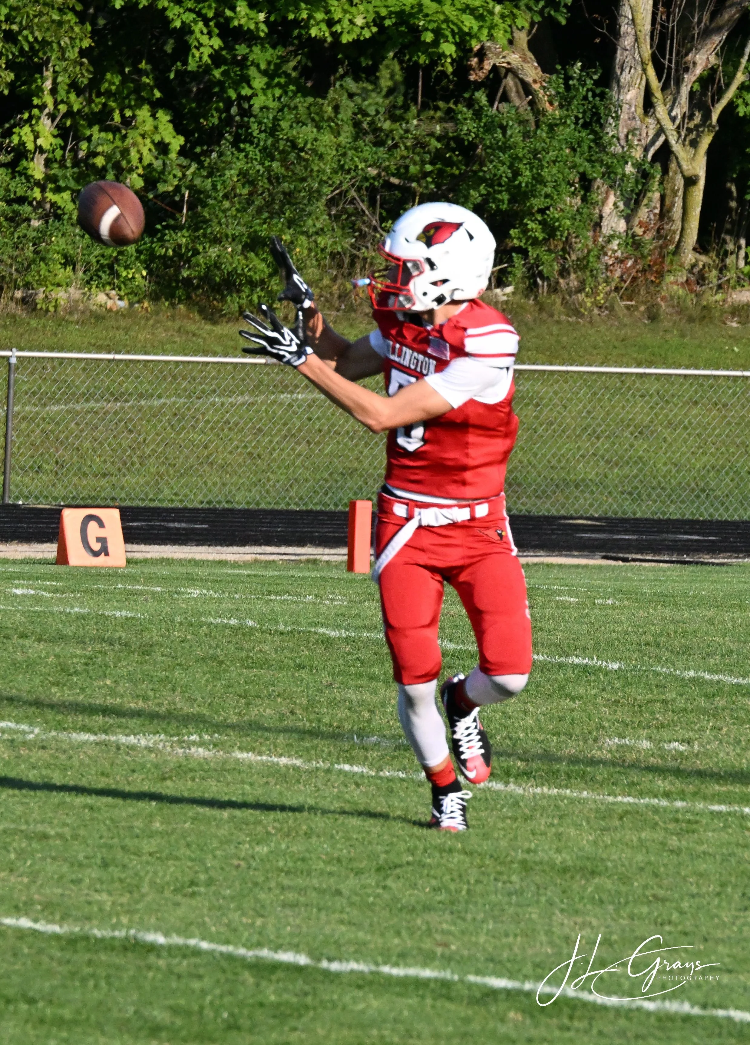 A football player in a red and white uniform with a helmet, catching a football on a football field.