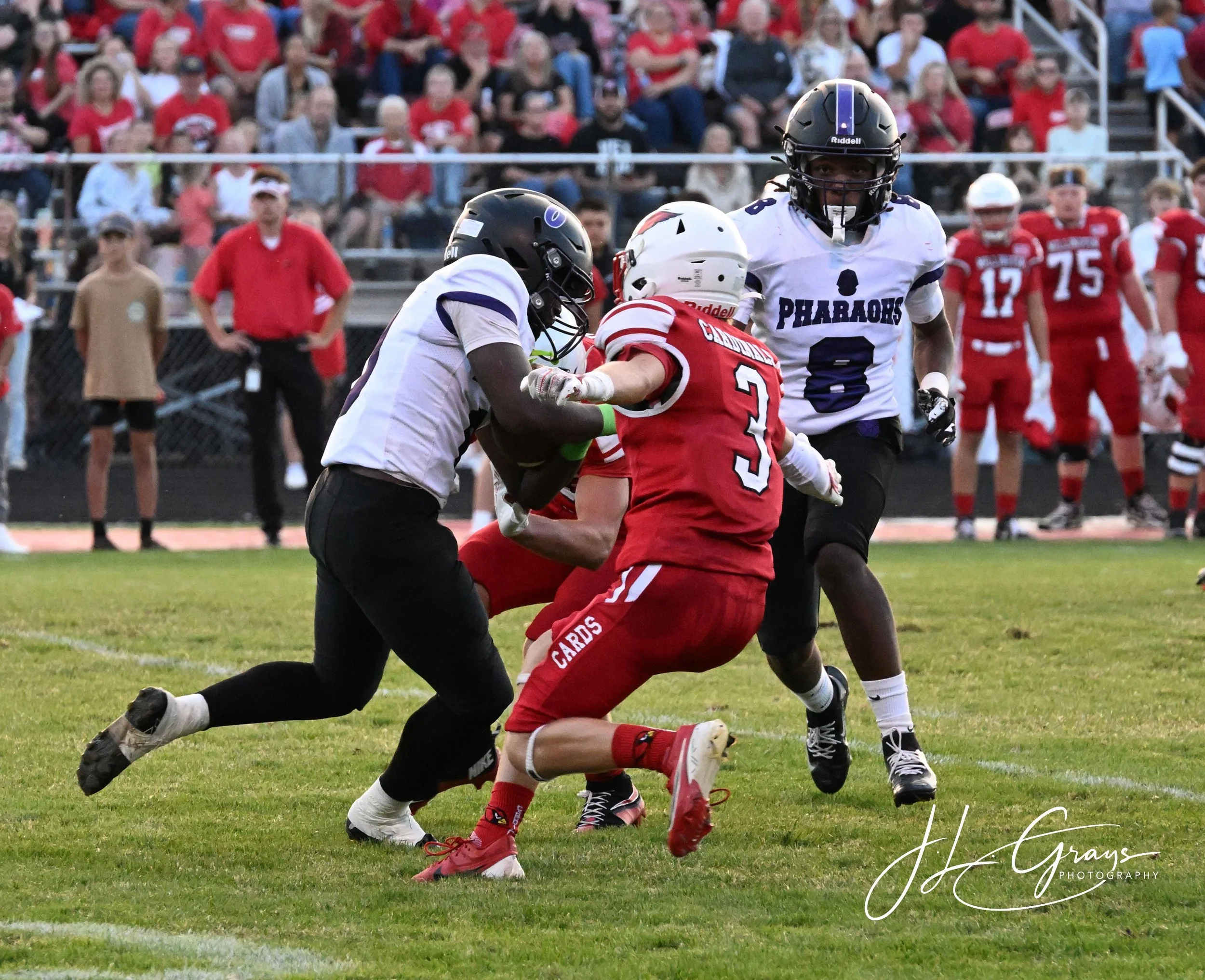 A football game with players tackling each other on the field, surrounded by a crowd of spectators.