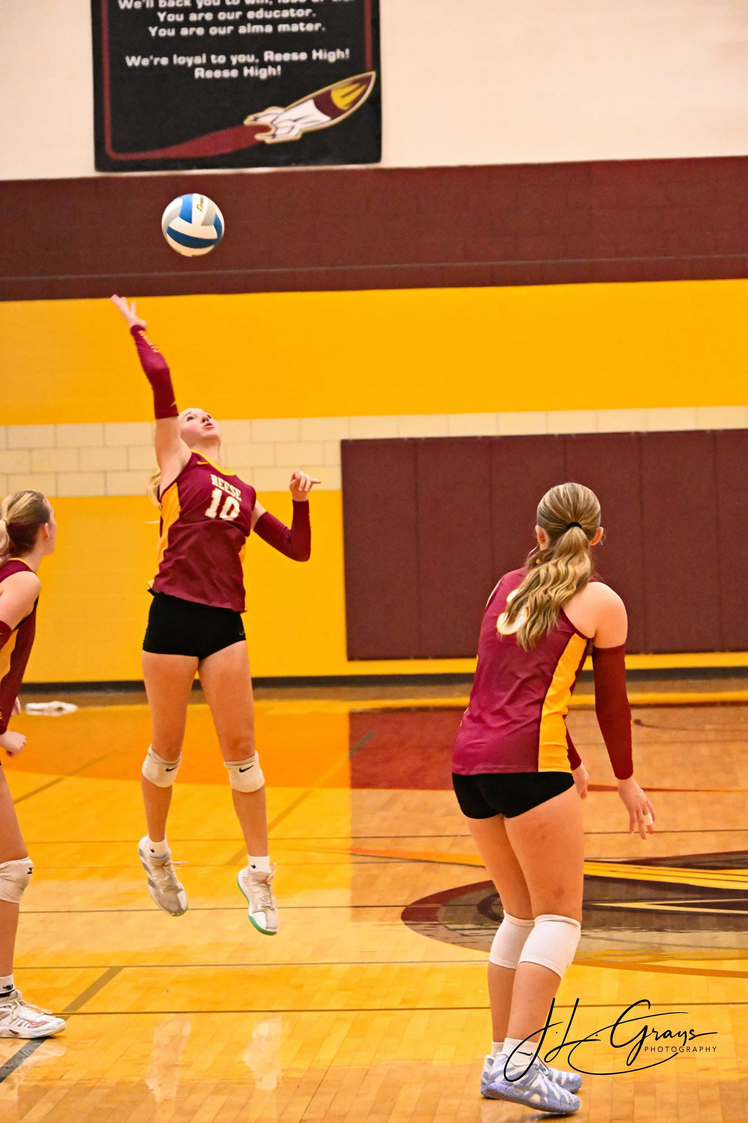 A volleyball player wearing a maroon and yellow jersey with the number 10 leaps to hit a volleyball during a game in a gymnasium with yellow and maroon walls.