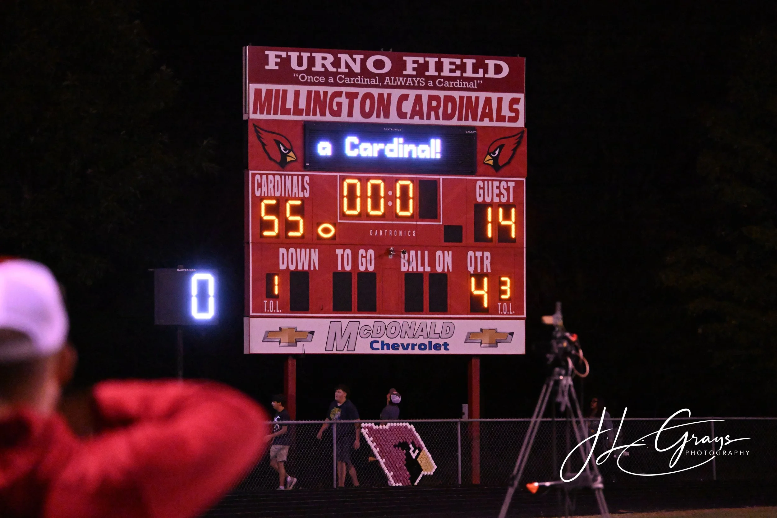 A digital scoreboard at a football game showing the score as 55 for the home team and 14 for the guest team, with the message 'a Cardinal!' displayed. The scoreboard has the stadium name 'Furno Field' and team name 'Millington Cardinals'.