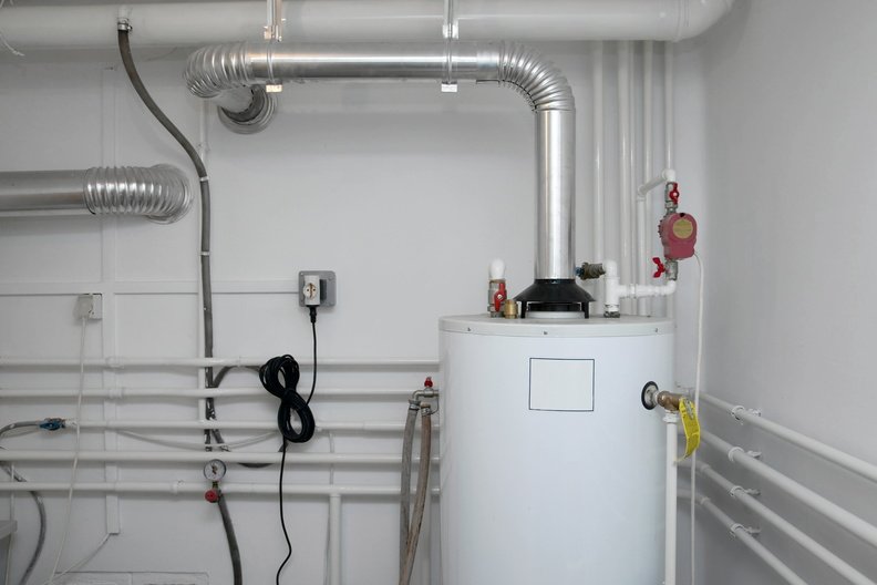 Industrial water heater with pipes, vents, and electrical connections in a utility room.