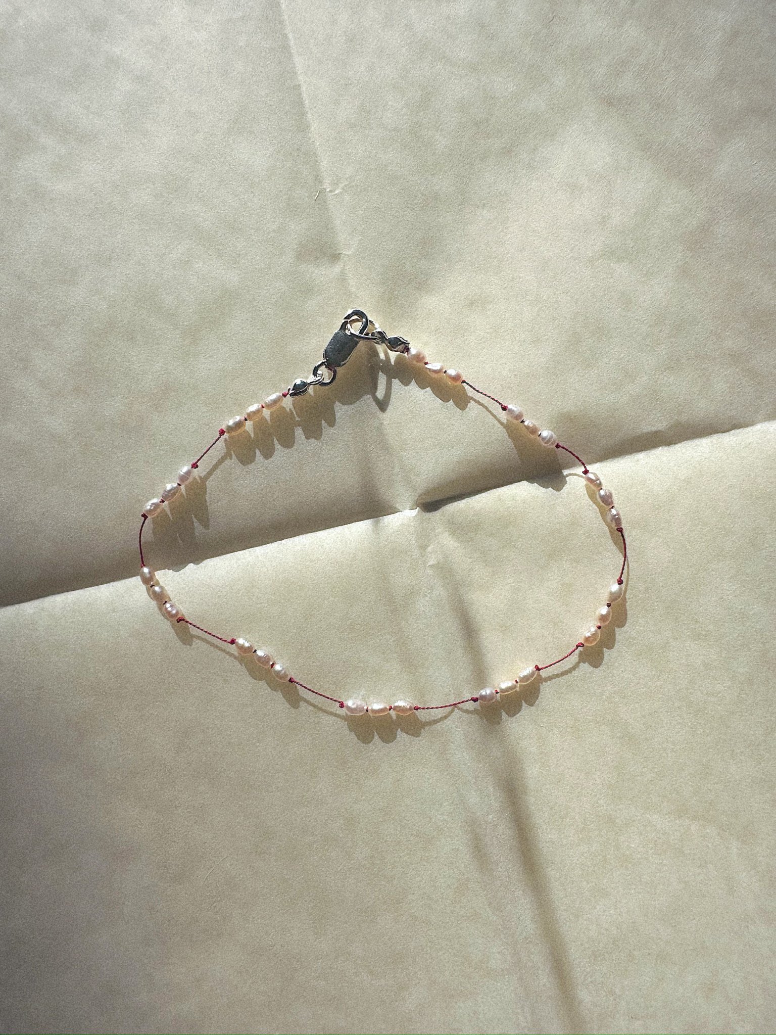 Anklet with tiny pearls knotted on red silk from above