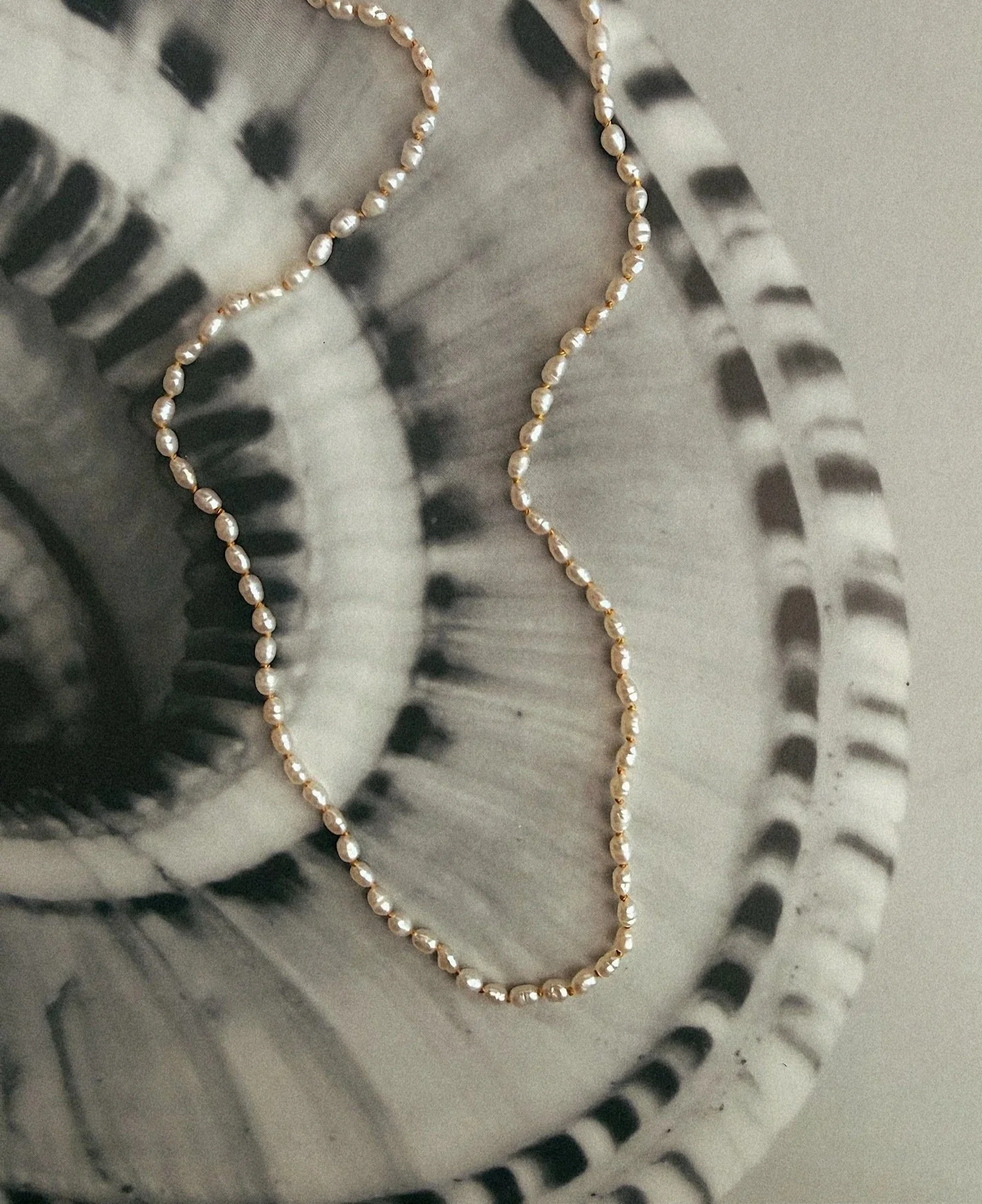 A pearl necklace resting on a metallic surface with a patterned design.