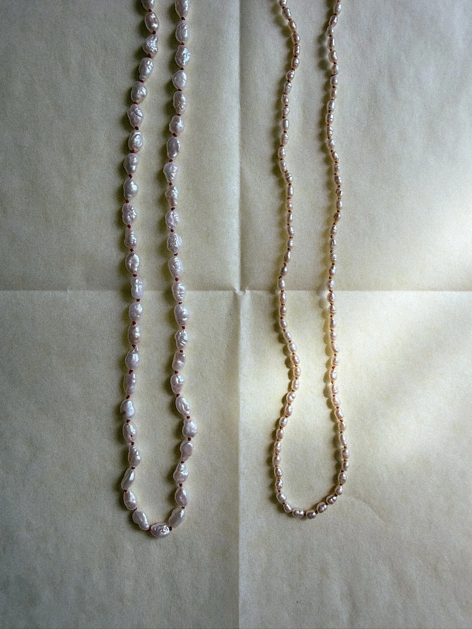 Two knotted pearl necklaces of different sizes draped side by side to show difference in pearl size