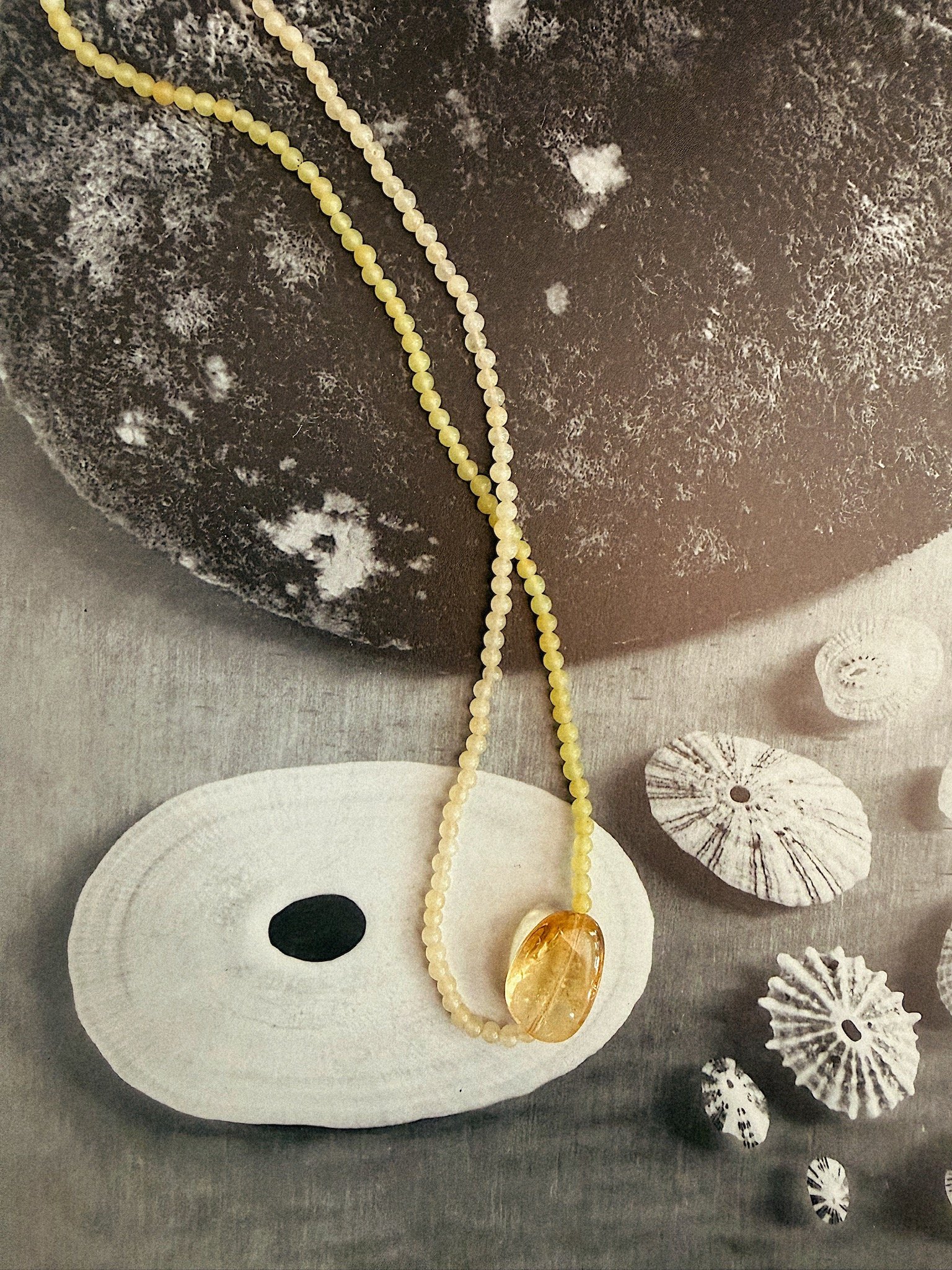 Two toned jade necklace with citrine pendent in middle shot on black and white patterned background