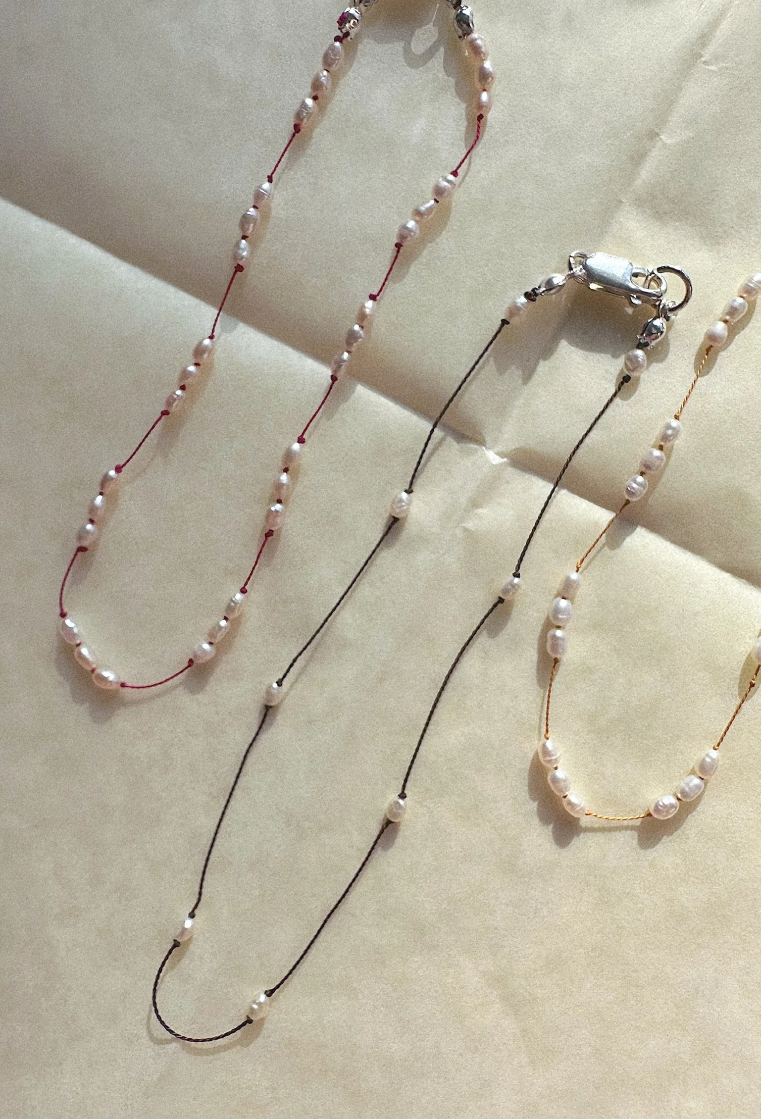 Three anklets draped next to each other. All with tiny pearls and different colors of silk