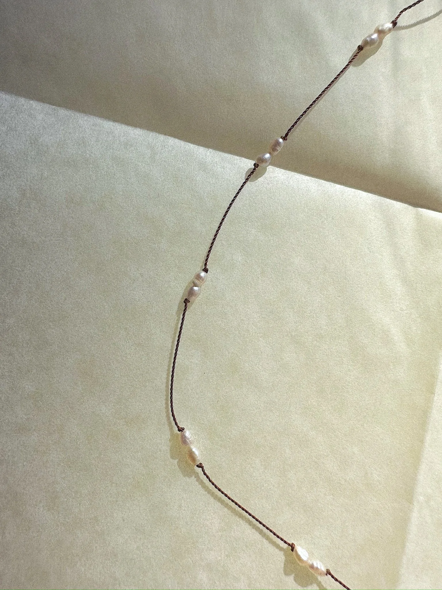 necklace overhead tight shot of pearls knotted on brown silk