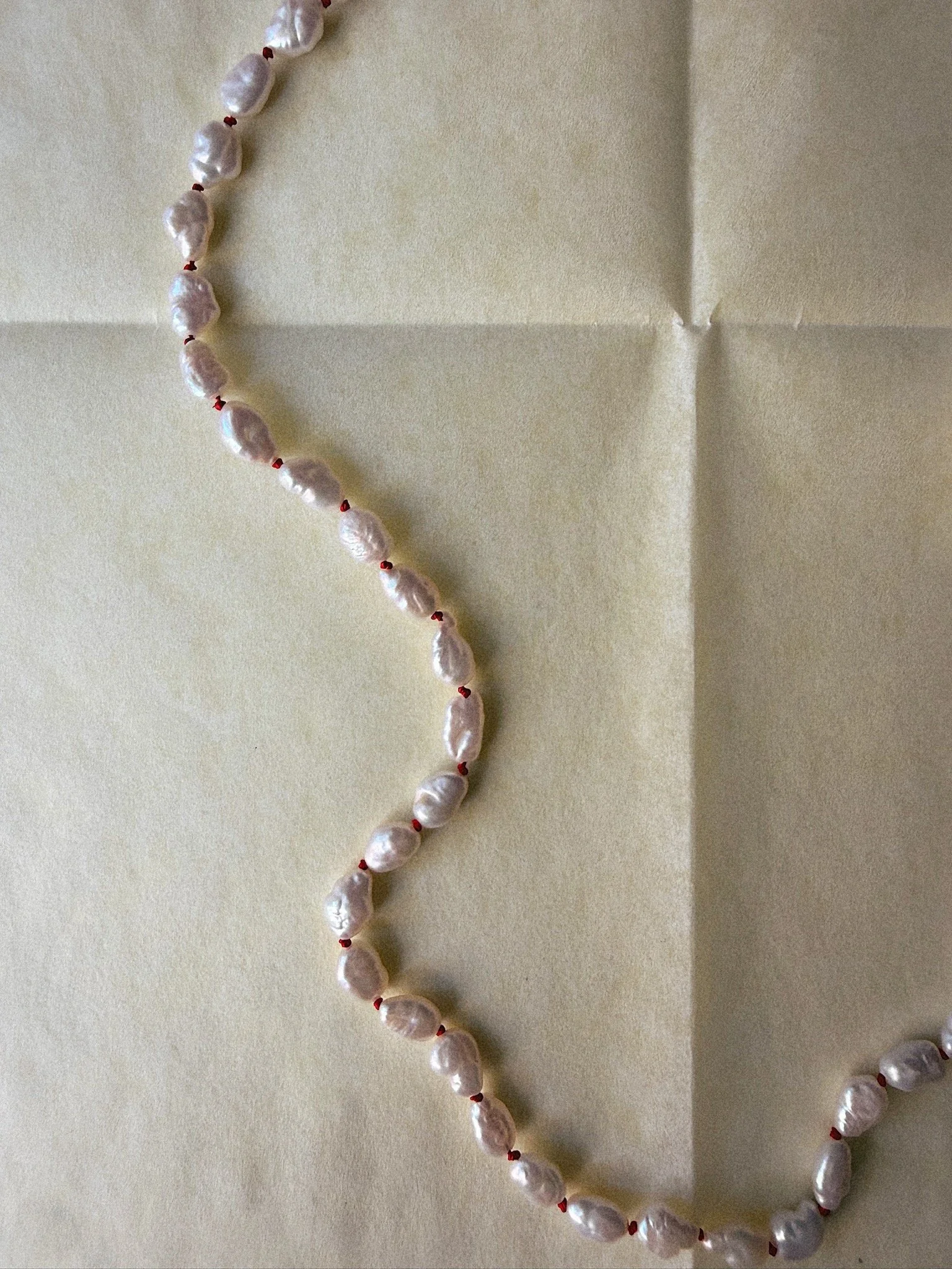 Close up of necklace with pearls knotted side by side on red silk