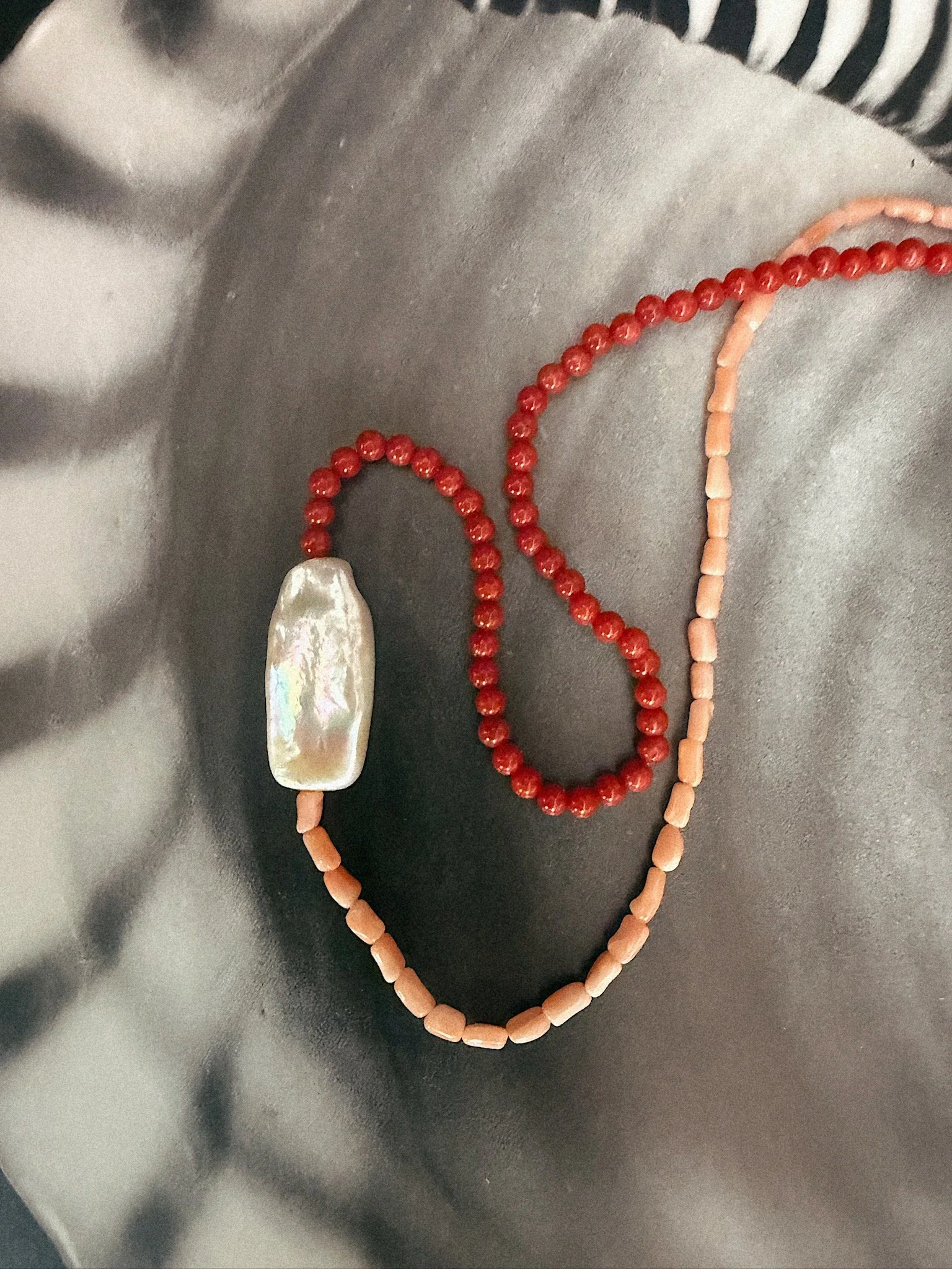 Two different shades of pink coral on necklace with large pearl pendent in middle photographed on black and white patterned background