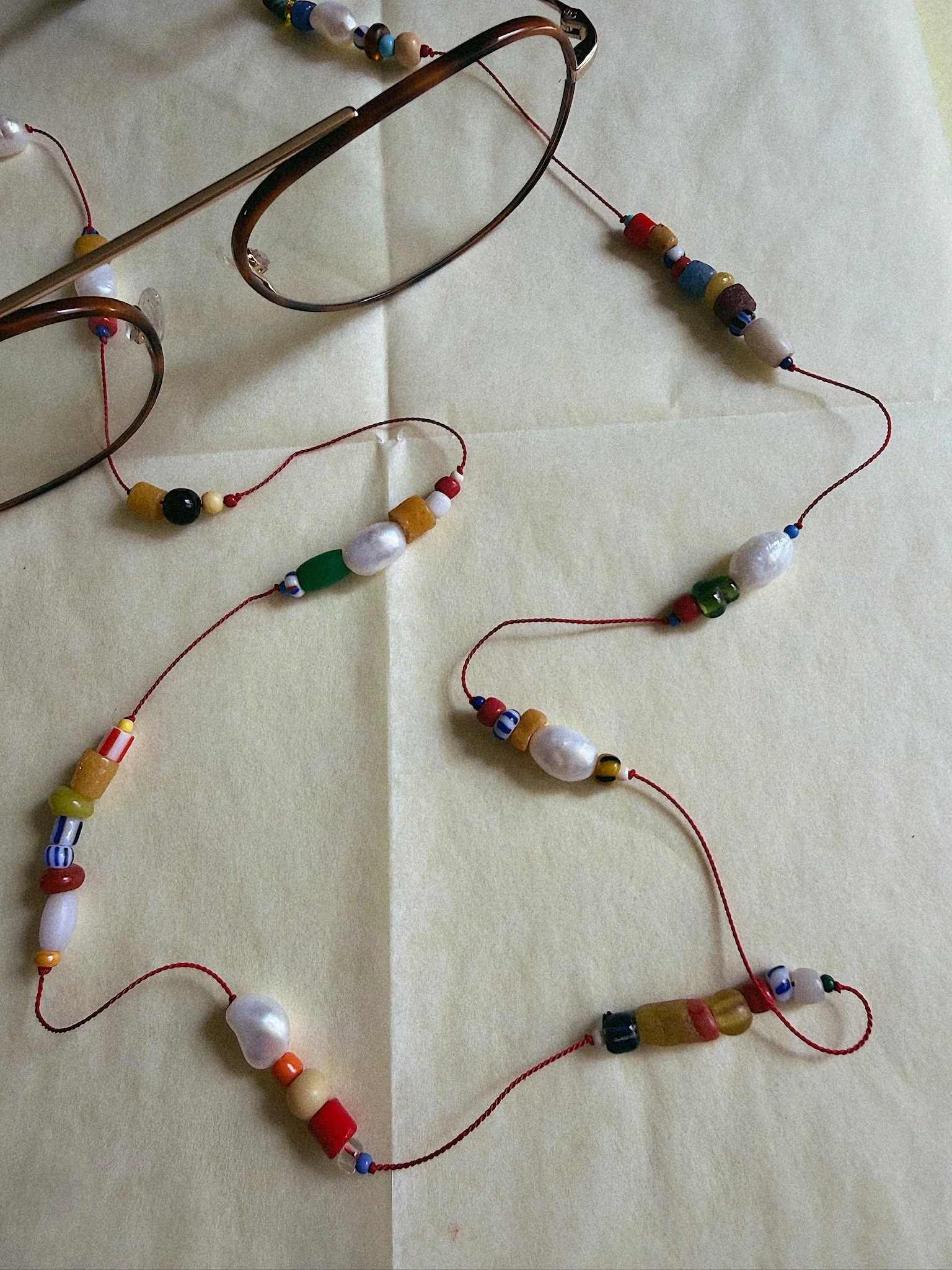 Red silk glasses chain with colorful beads and pearls shown on reading glasses from above