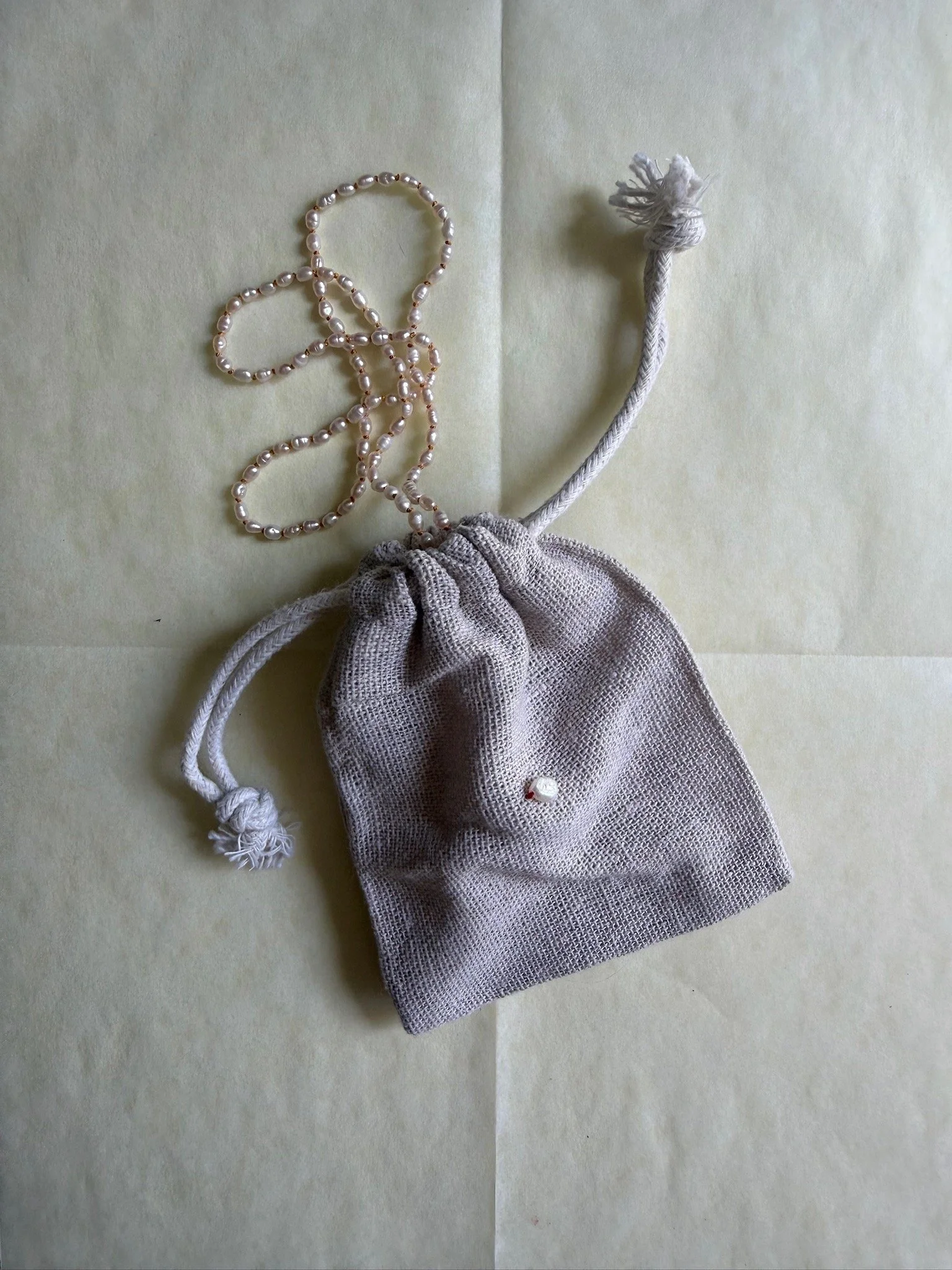 Petite pearl necklace knotted side by side on silk shown coming out of linen jewelry bag