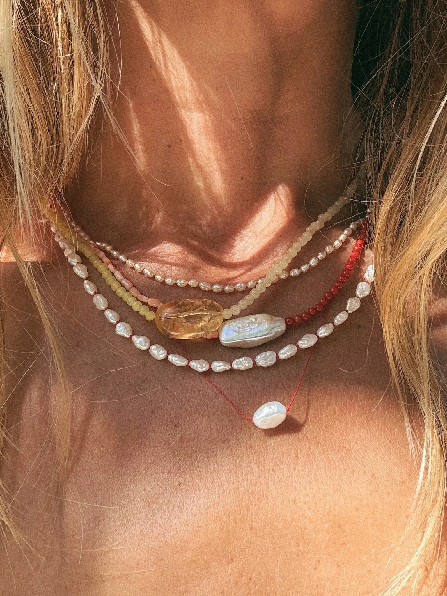 Close up photo of neck, hair, chest with multiple stacked colorful pearl and gem necklaces