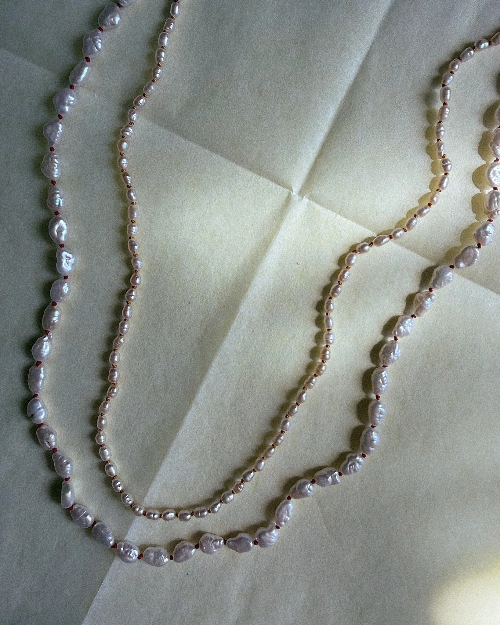 Two pearl necklaces shown together, one with smaller pearls knotted on silk and one with larger pearls knotted on silk
