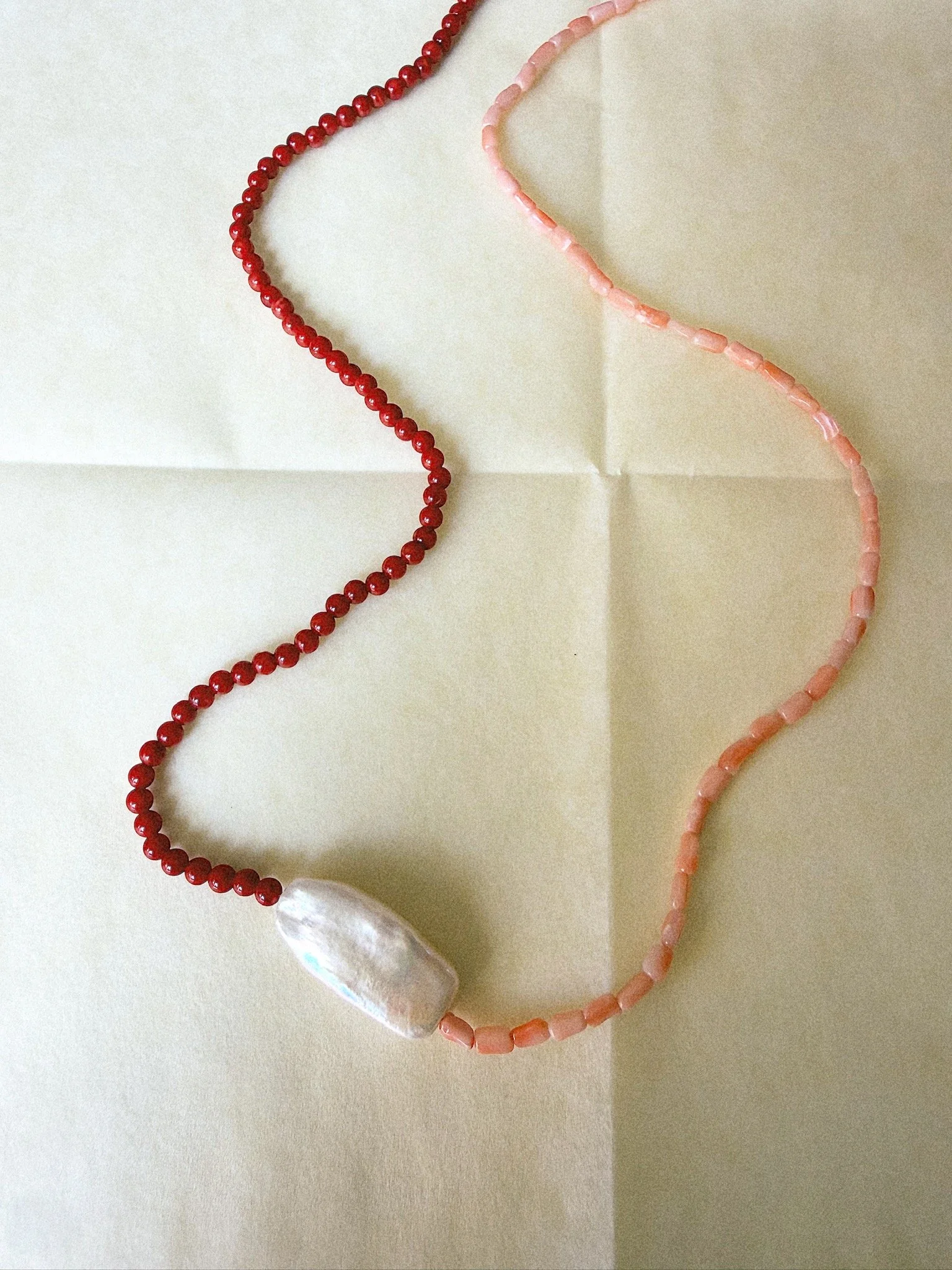 Two different shades of pink coral on necklace with large pearl pendent in middle