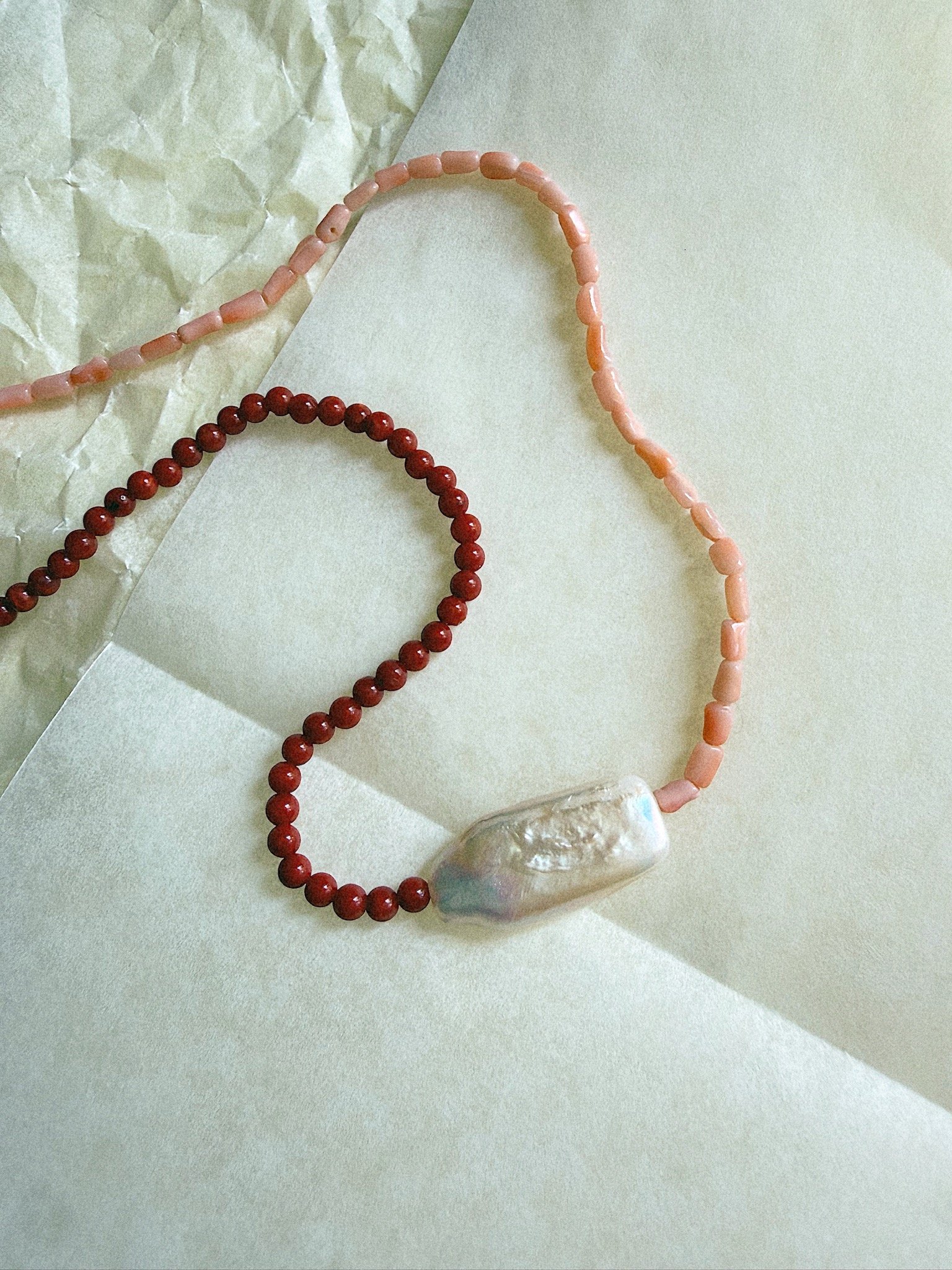 Tighter shot of Two different shades of pink coral on necklace with large pearl pendent in middle