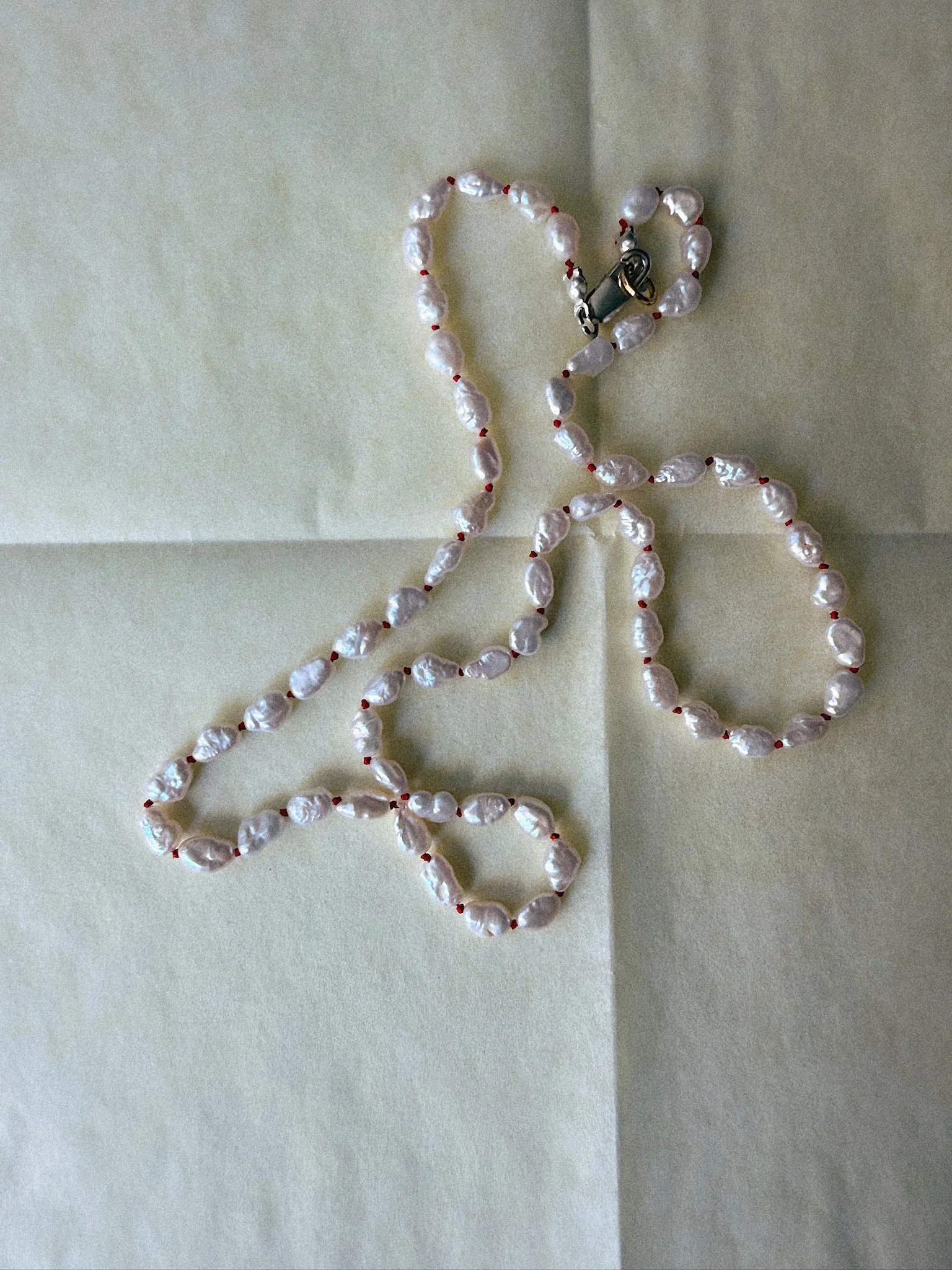 Necklace with pearls knotted side by side on red silk and silver clasp draped organically