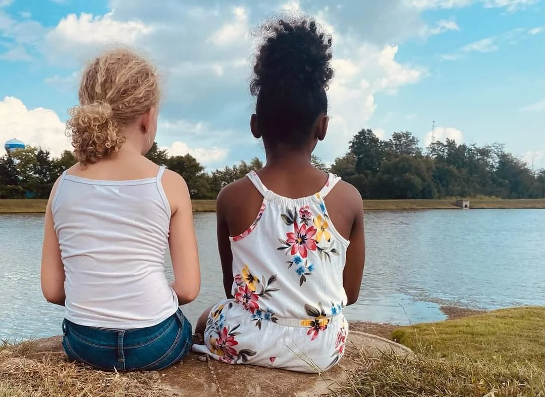 Two girls sitting together by a lake