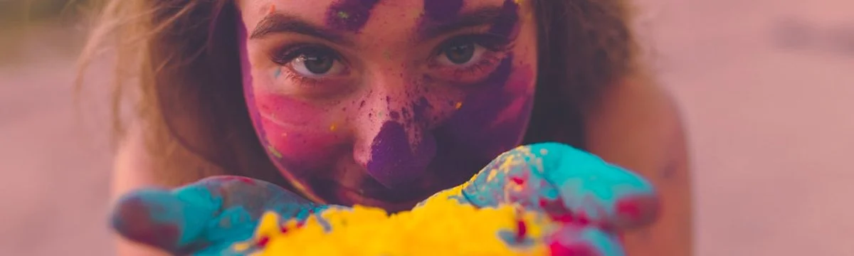 Close-up of a woman's face and hands covered in colorful Holi paint