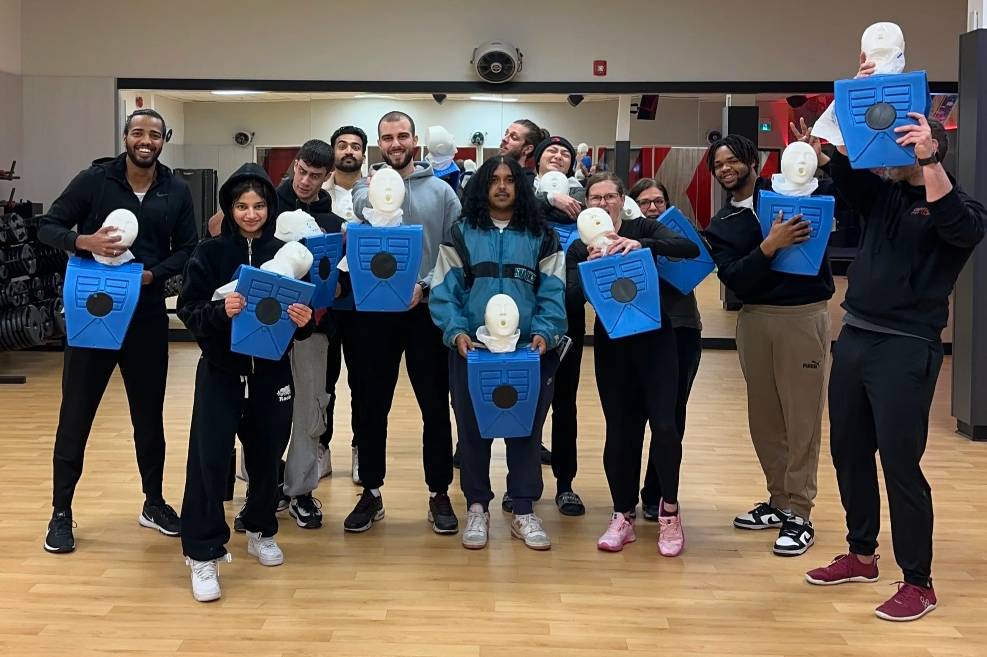Group of people holding CPR mannequin heads and face shields in a gym studio.