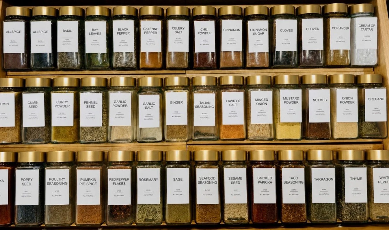 A wooden spice rack with glass jars filled with various spices and herbs, each labeled with its name.
