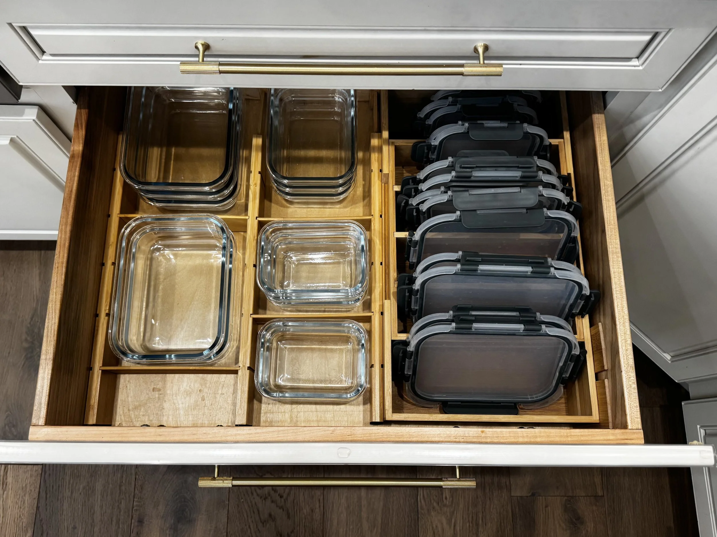 Open kitchen drawer filled with glass storage containers and black plastic lids.