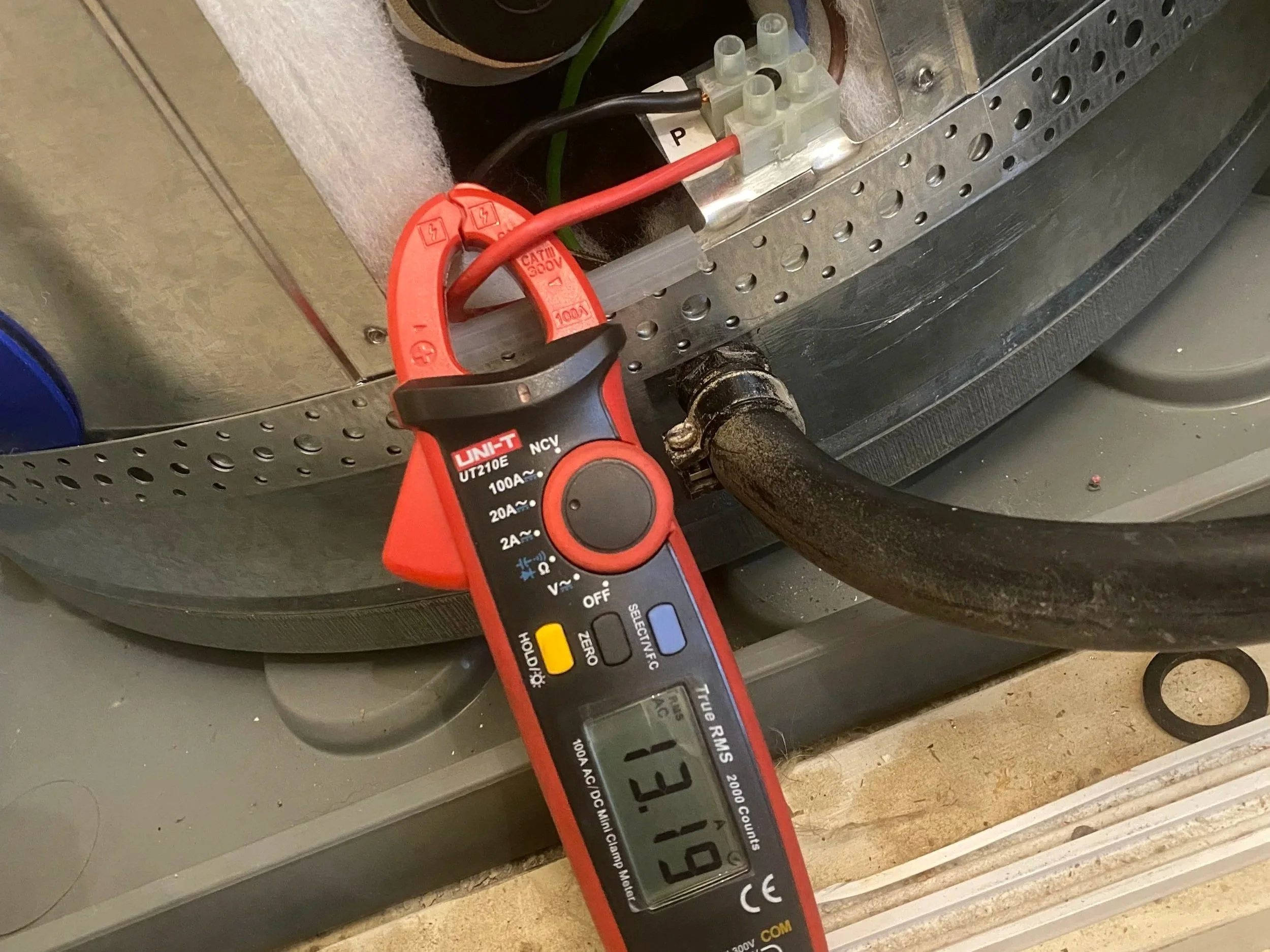 A digital multimeter measuring a circuit with wires connected to a metal panel and electrical components.