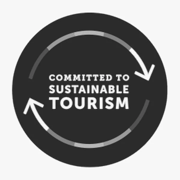 Black circular badge with white arrows forming a loop around the text "Committed to Sustainable Tourism."