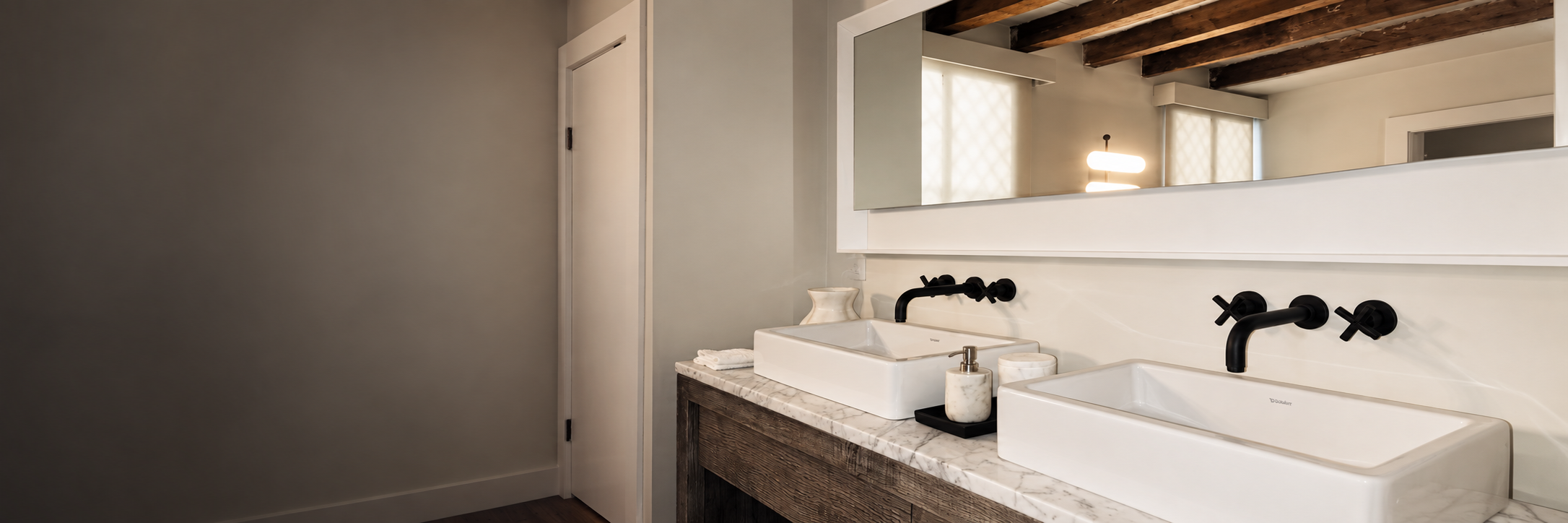 Bathroom vanity with two white sinks and black wall-mounted faucets