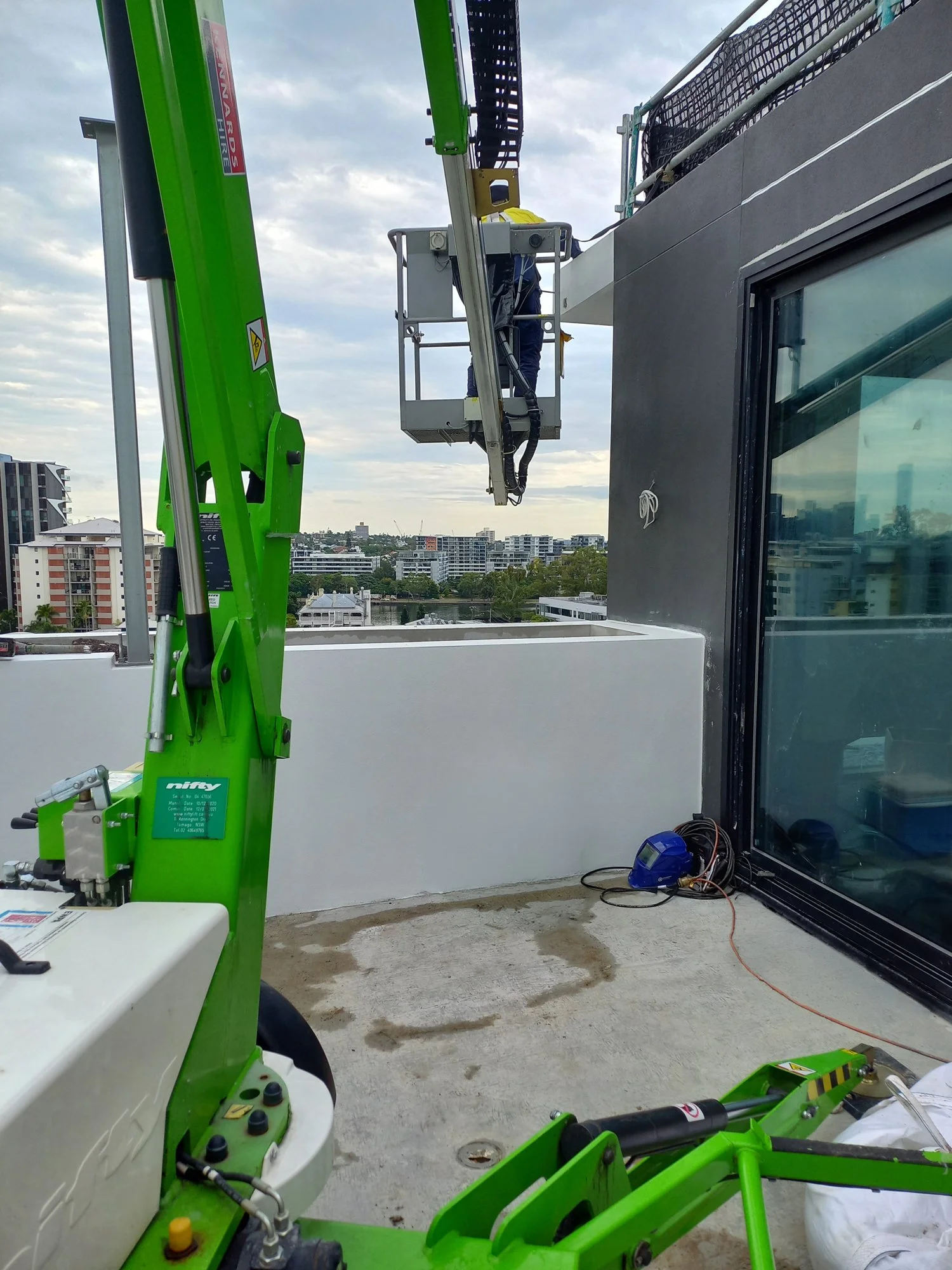 A worker on a hydraulic lift working on a building's exterior, with city buildings in the background.