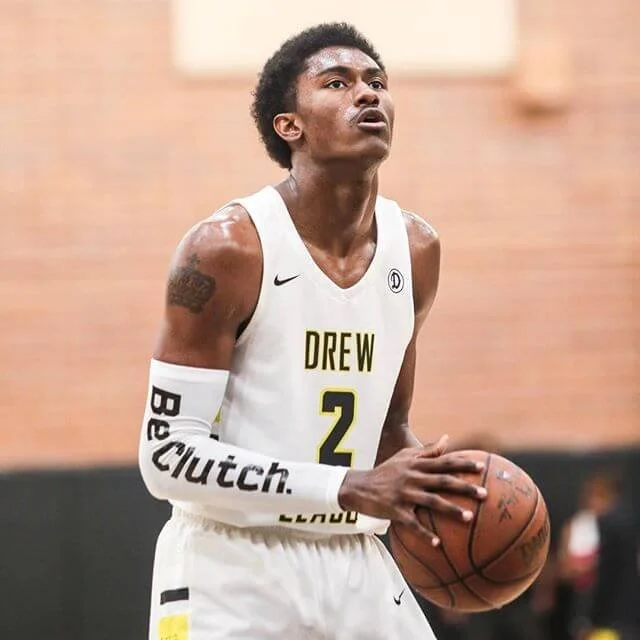 Ron Artest III, a basketball player wearing a white jersey with the words 'DREW' and the number 2, holding a basketball, standing on the court during a game.