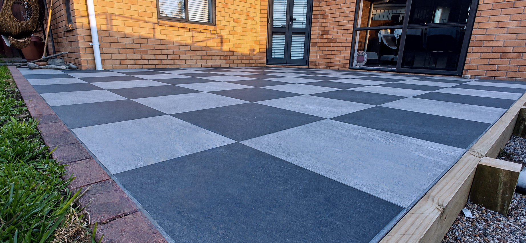Checkered black and white tiled patio outside a brick house with black-framed doors and windows.