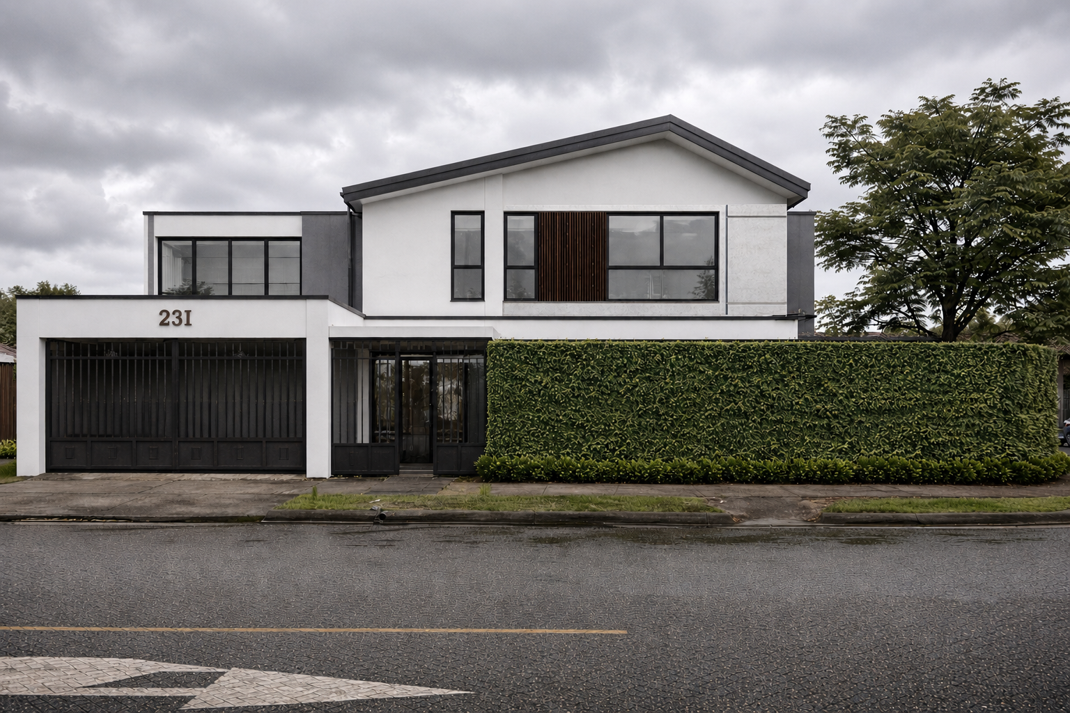 Modern two-story house painted white with black accents and a large green hedge in front, numbered 231, on a rainy day with dark clouds in the sky.