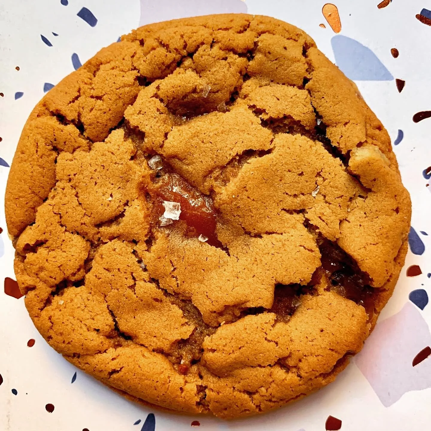 A large chocolate chip cookie with broken pieces of cookie showing chocolate chips inside, on a decorative paper plate.