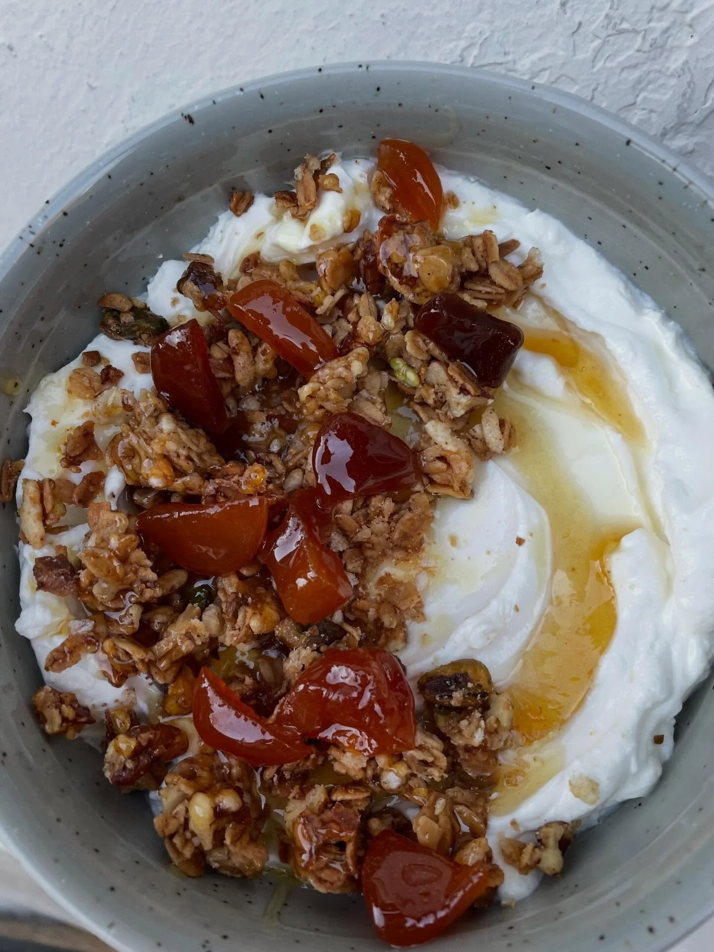Close-up of a bowl of yogurt topped with granola, cherry tomatoes, honey, and a drizzle of honey.
