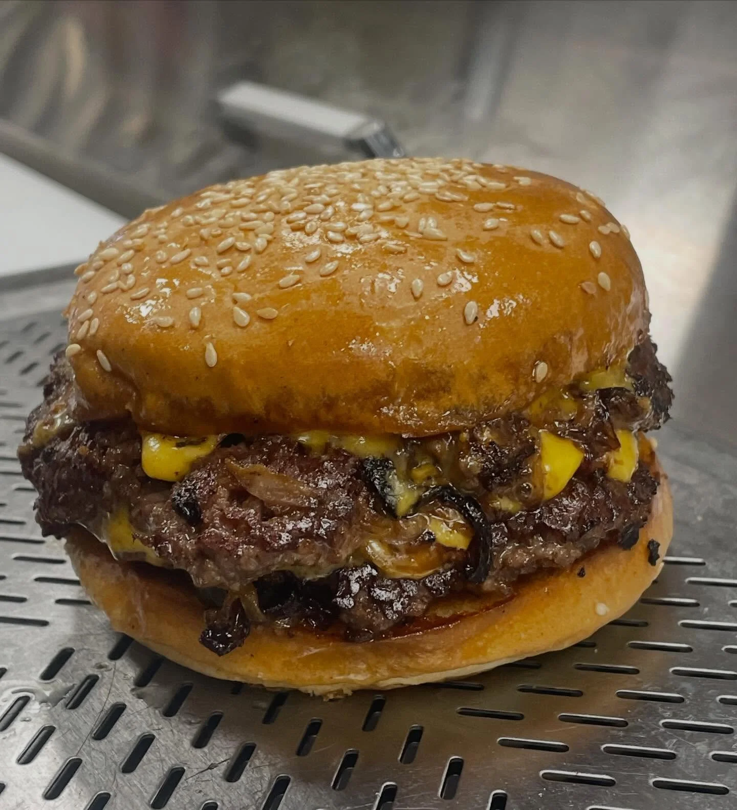 Close-up of a cheeseburger with a sesame seed bun, melted cheese, and cooked beef patty on a metal surface.