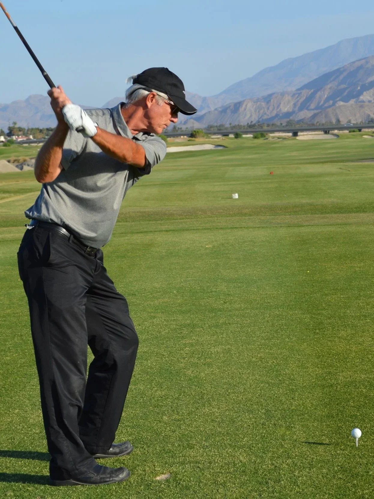 PGA Master Professional Dave Cahill playing golf on a golf course, preparing to hit a golf ball with a club, in a scenic area with mountains in the background.