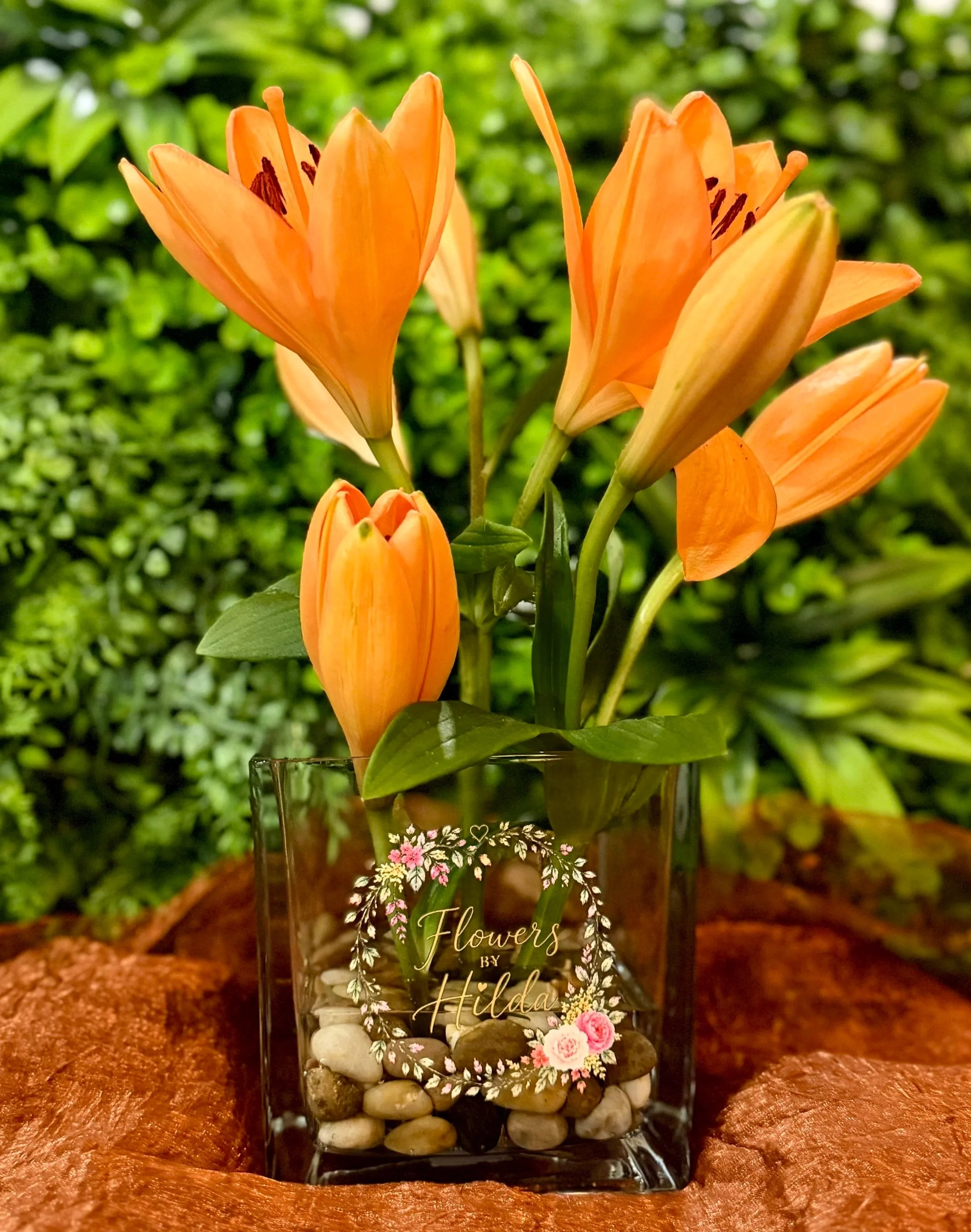 Orange lilies in a square glass vase filled with river stones