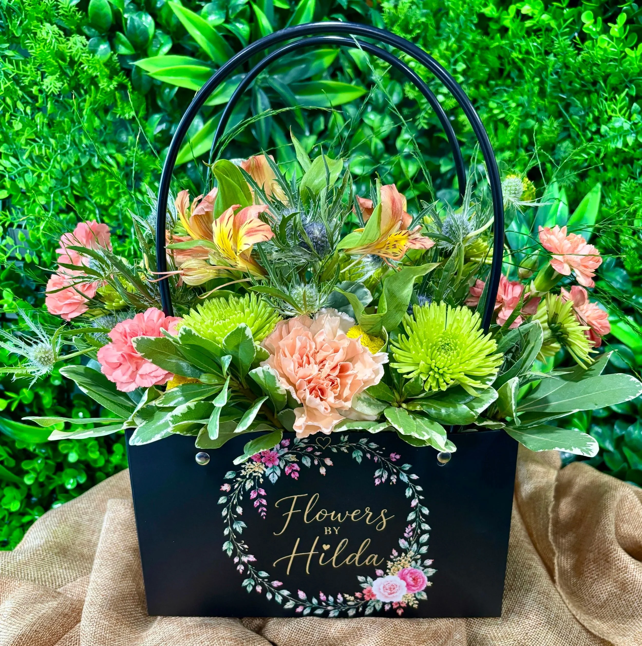 Carnations, green chrysanthemums and alstroemeria in a black Flowers by Hilda gift bag