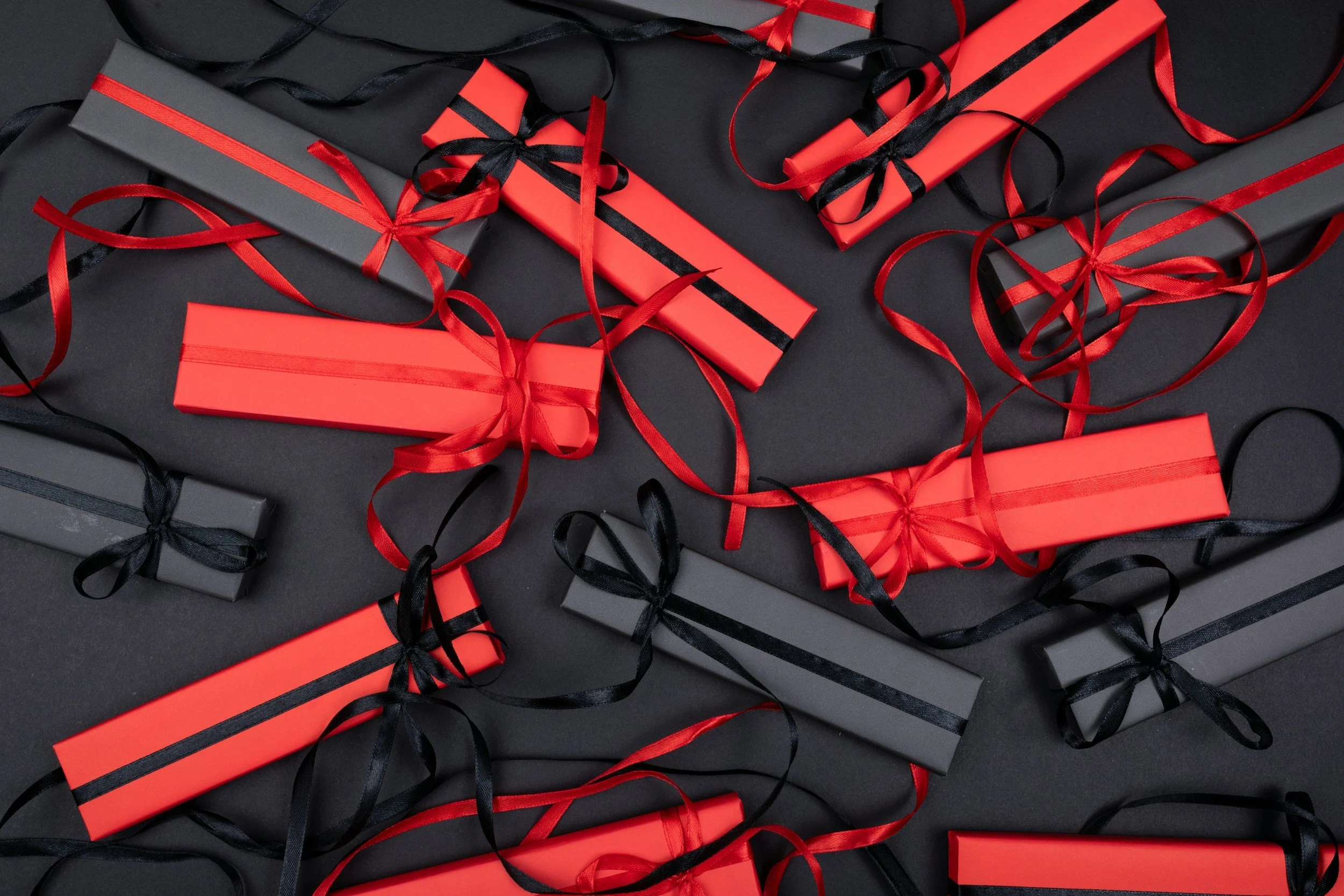 Black and red gift boxes wrapped with black and red ribbons, scattered on a black background.