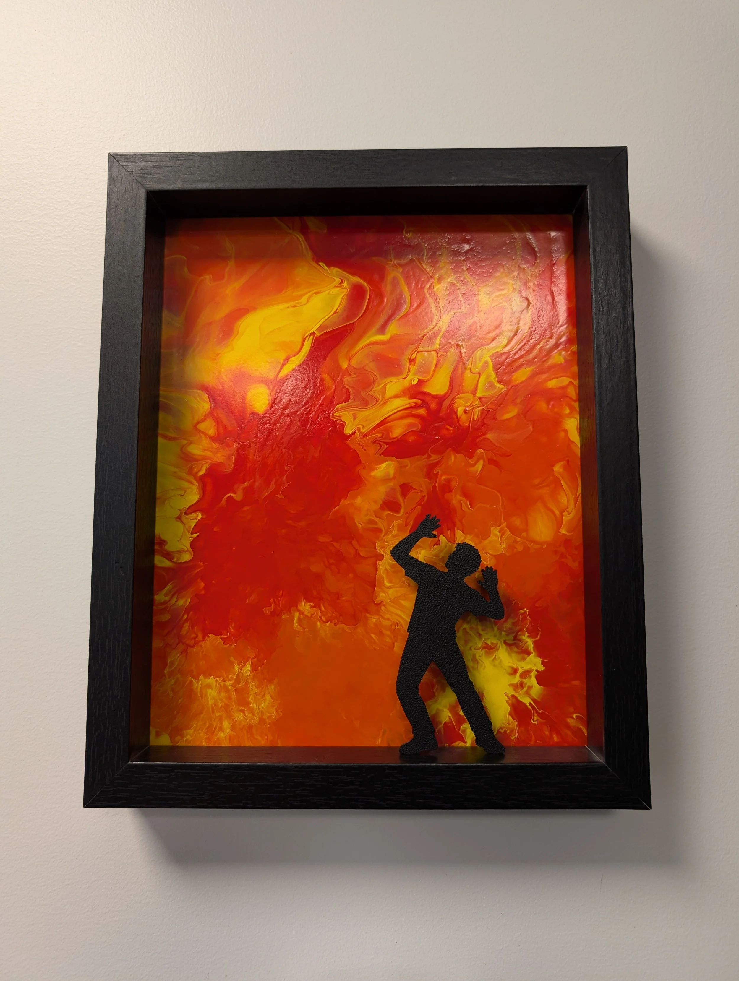 A black framed painting containing swirls of reds, oranges, and yellows with a startled black silhouette in the foreground.