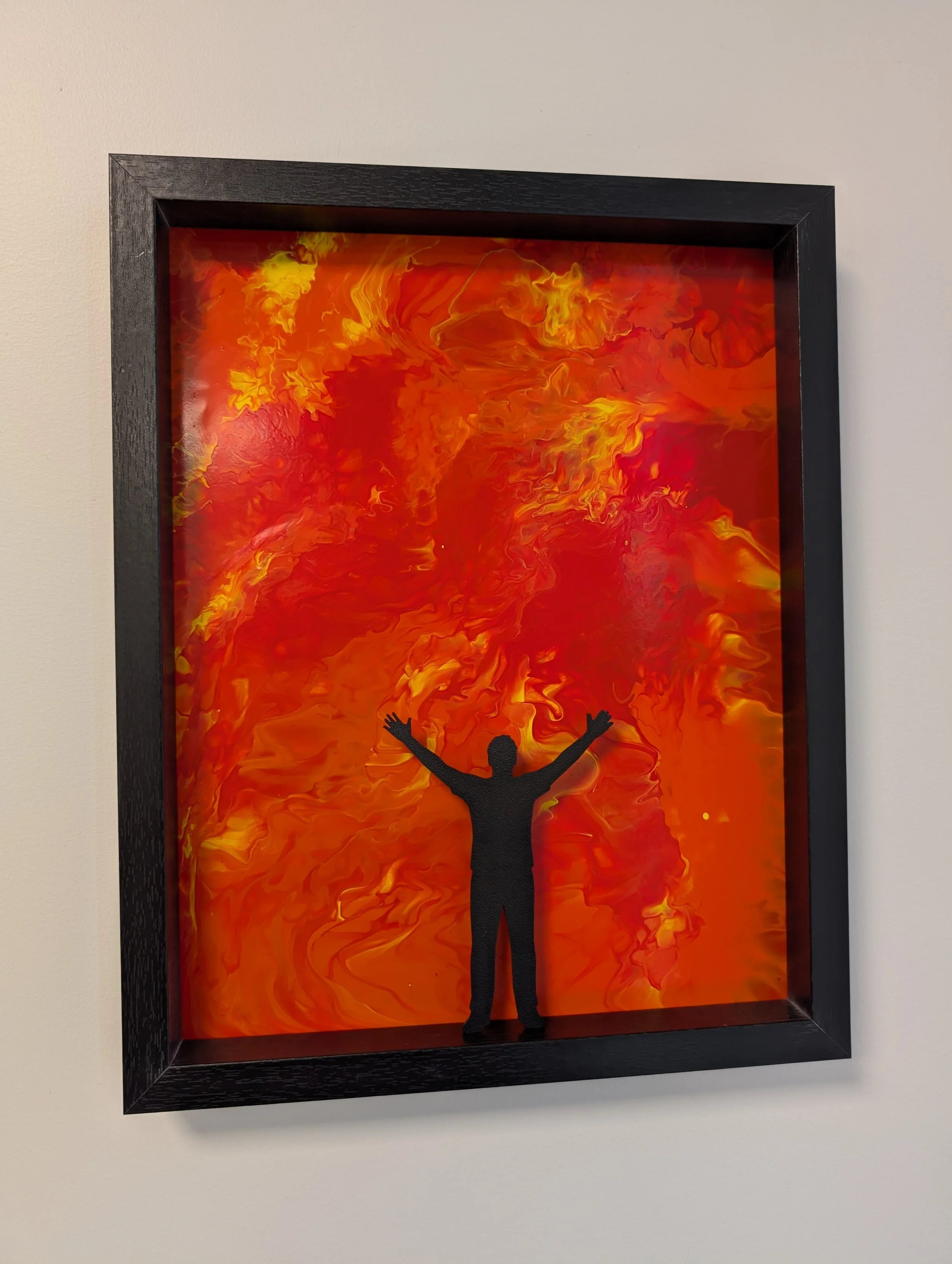a black framed painting containing swirling reds, oranges, and yellows, with a black silhouette in the foreground with arms outstretched accepting the inevitable arrival of the storm.