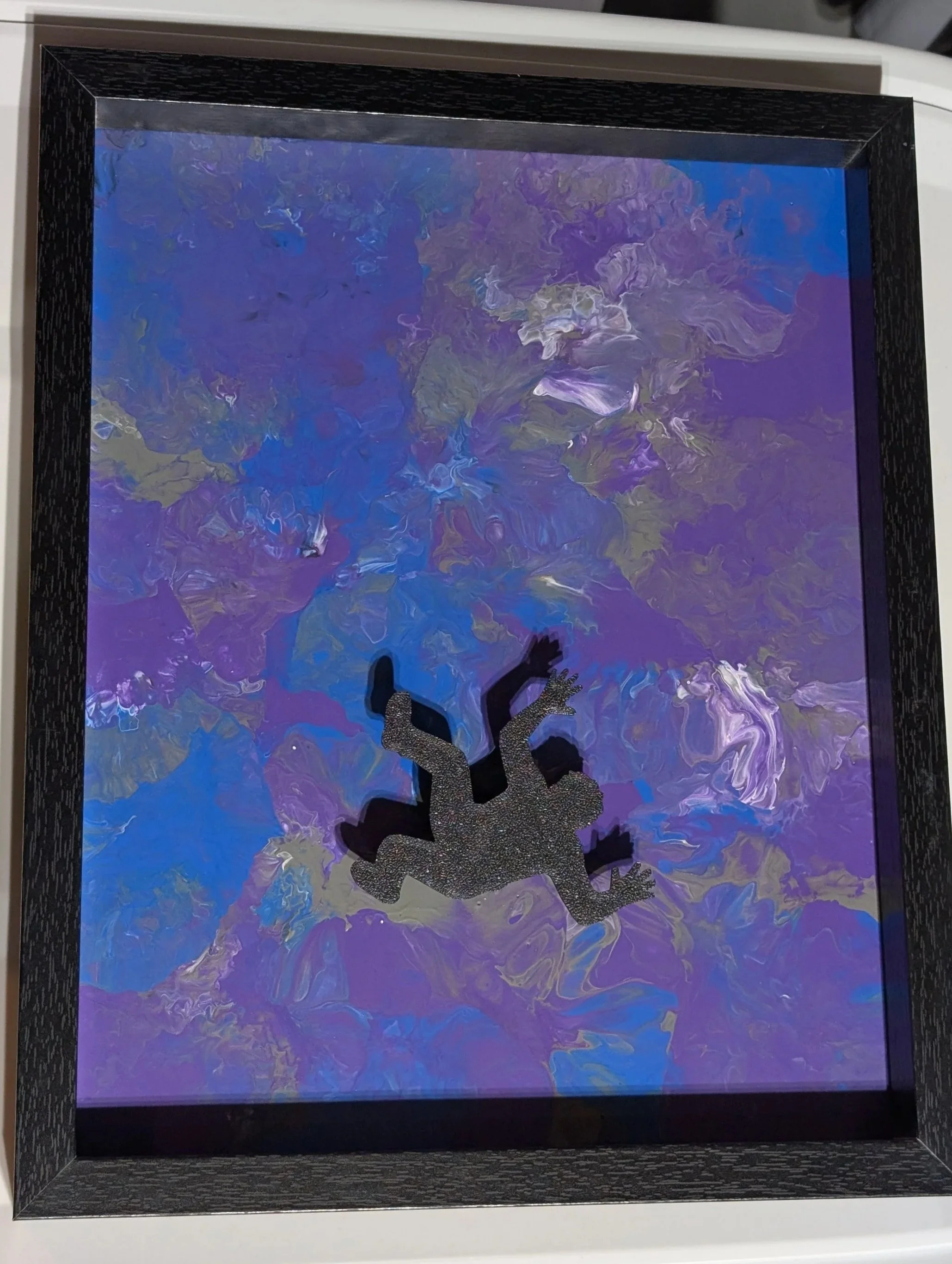 A black framed painting filled with swirling blues, purples, and greys.  An offset 3D printed silhouette of a falling figure is in the bottom third of the painting.
