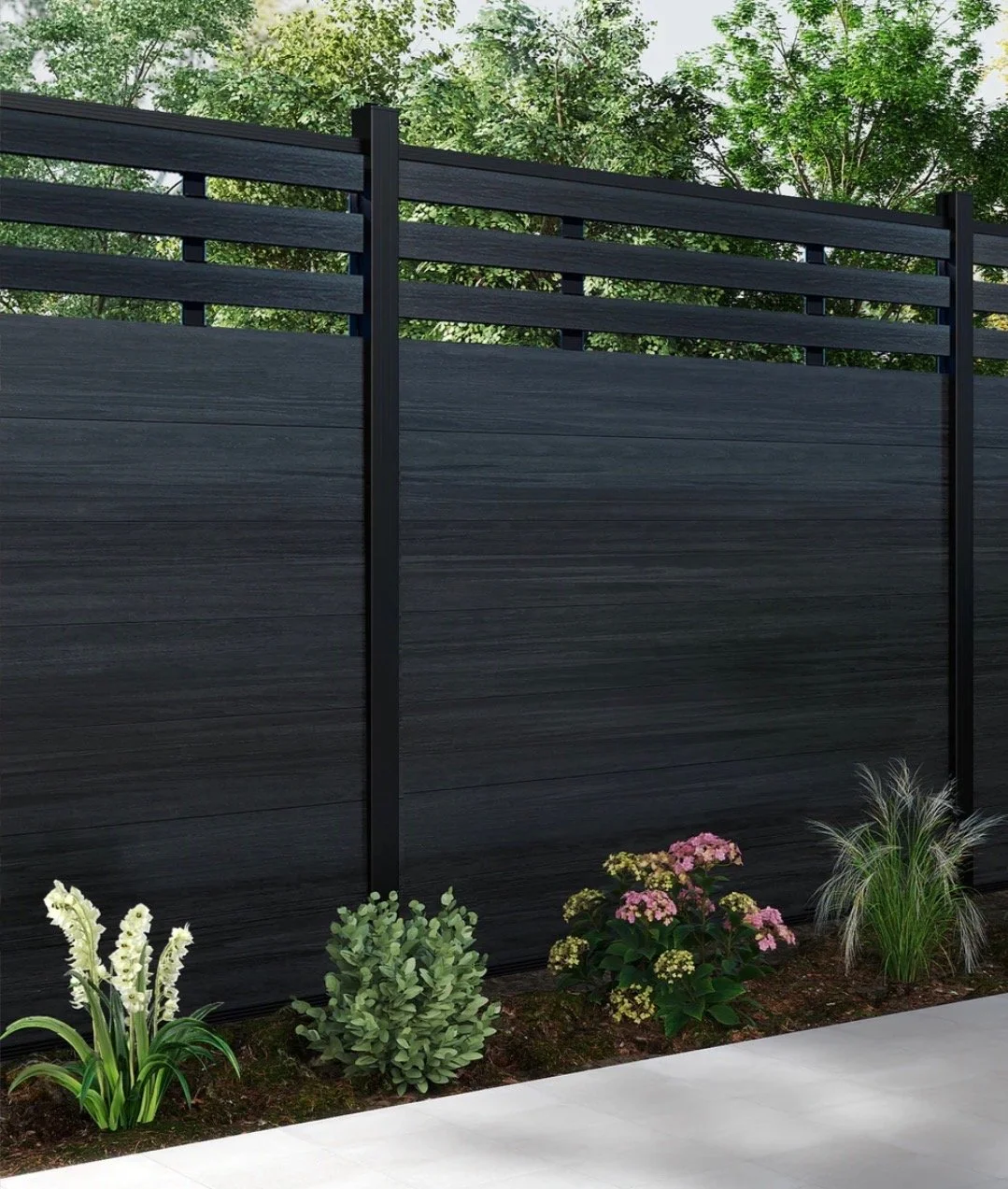 Black modern privacy fence with horizontal slats, surrounded by flowers and greenery, with a concrete walkway in front and trees in the background.