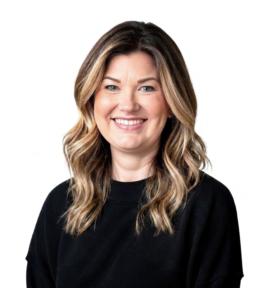 A smiling woman with wavy, shoulder-length brown hair wearing a black top against a white background.