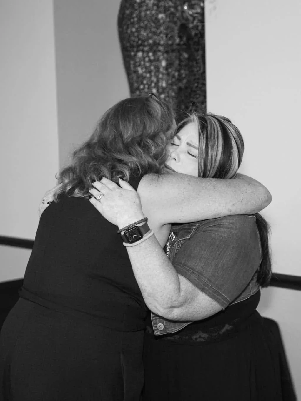 Two women hugging each other, one with curly hair and the other with straight hair, in a heartfelt embrace.