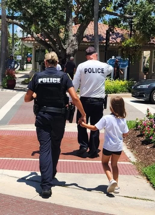 A police officer and a police officer in uniform walking hand in hand with a young girl on a city sidewalk.